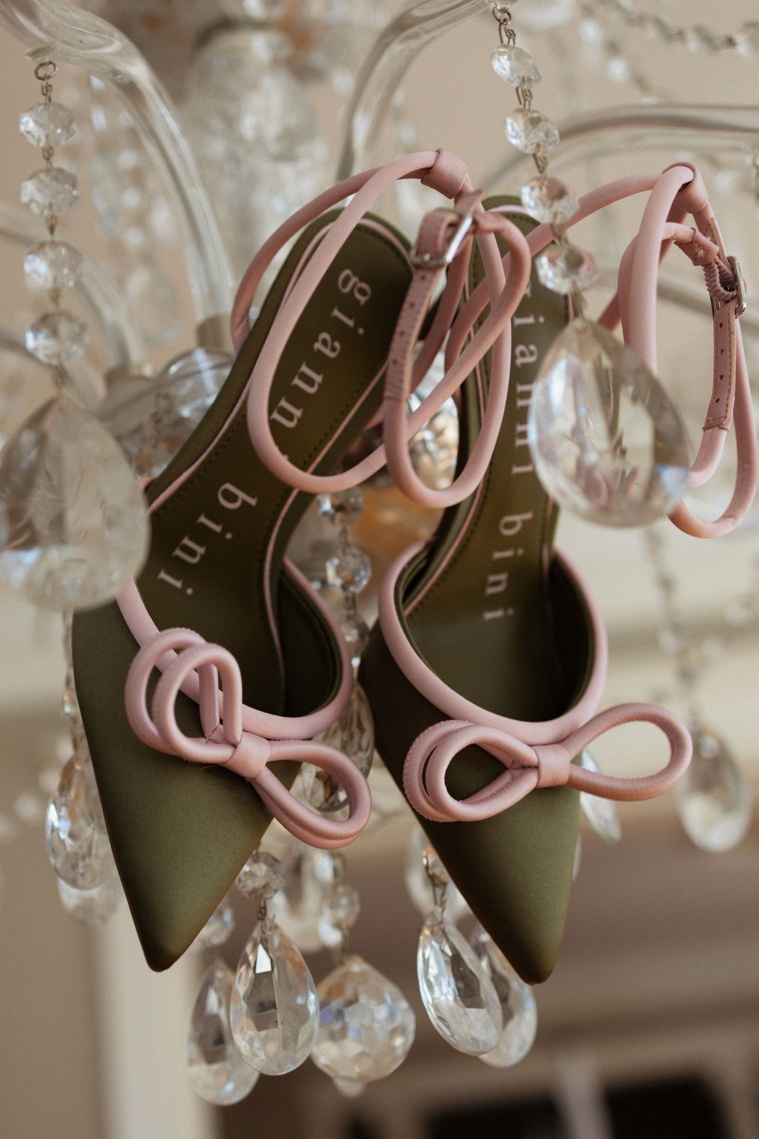 Multiple images of elegant pink and black slingback heels hanging from a crystal chandelier in soft lighting.