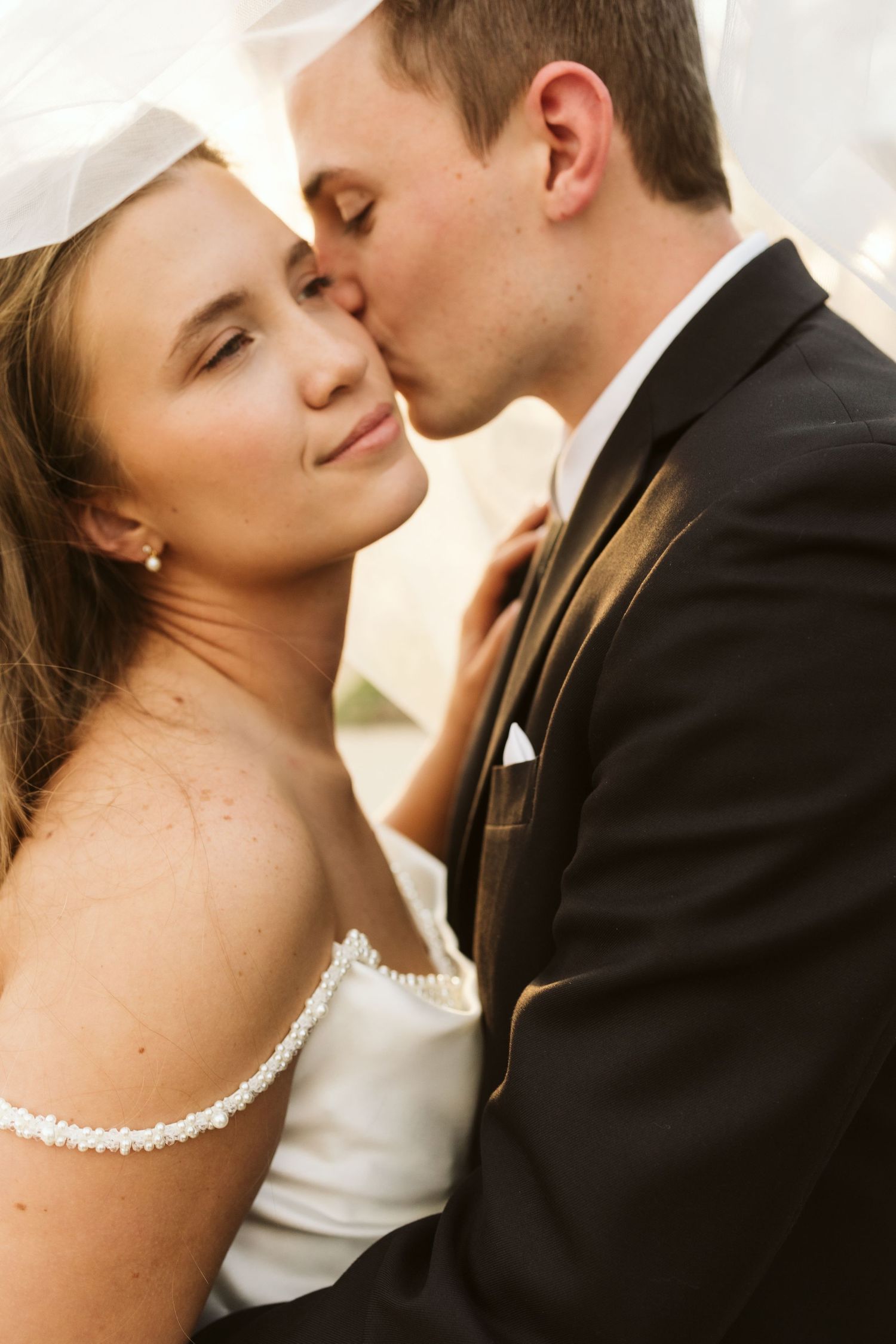 A romantic wedding moment with a bride in white dress and groom in black suit sharing a tender kiss.