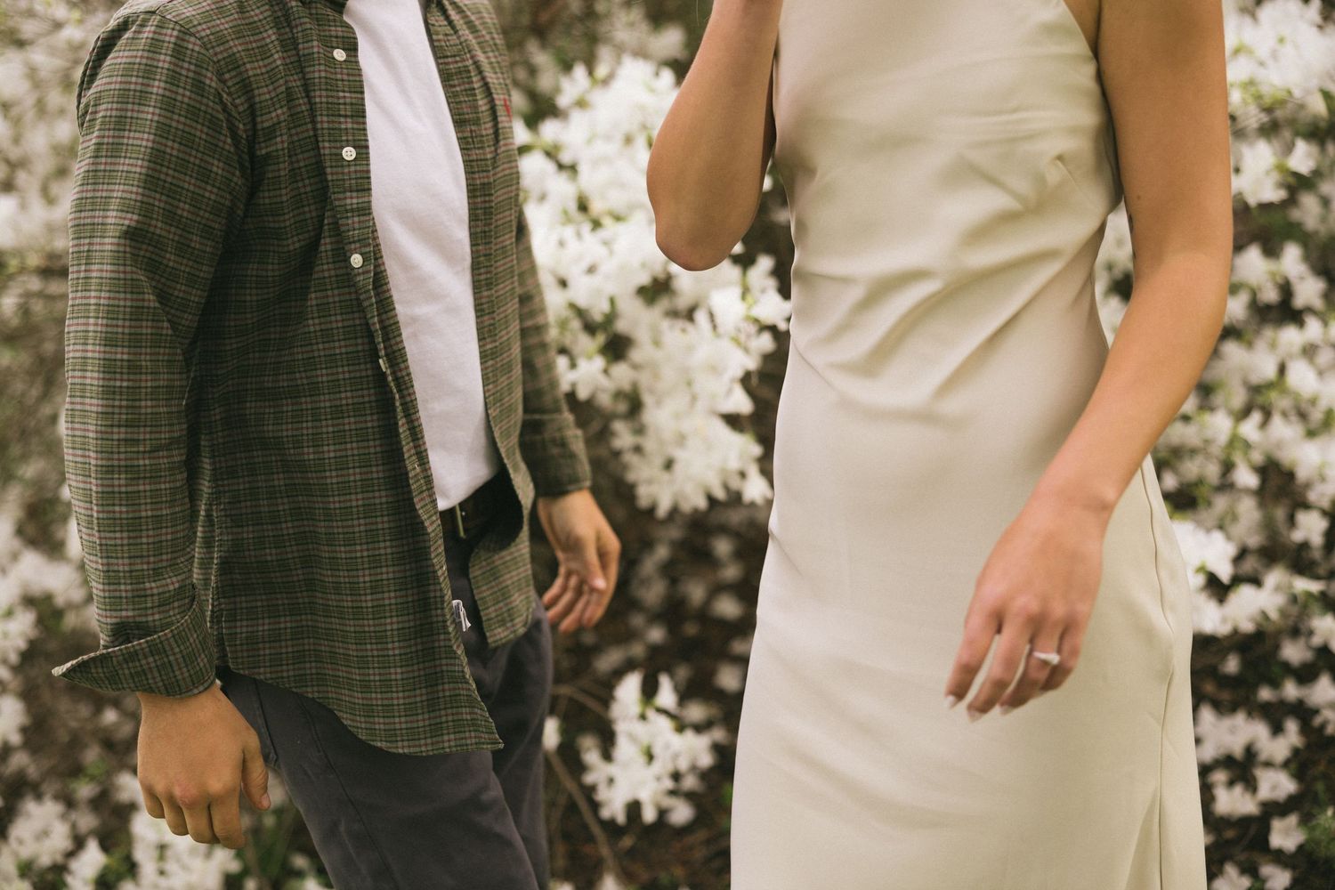 A couple in contrasting outfits of plaid and white stand together in a garden setting.