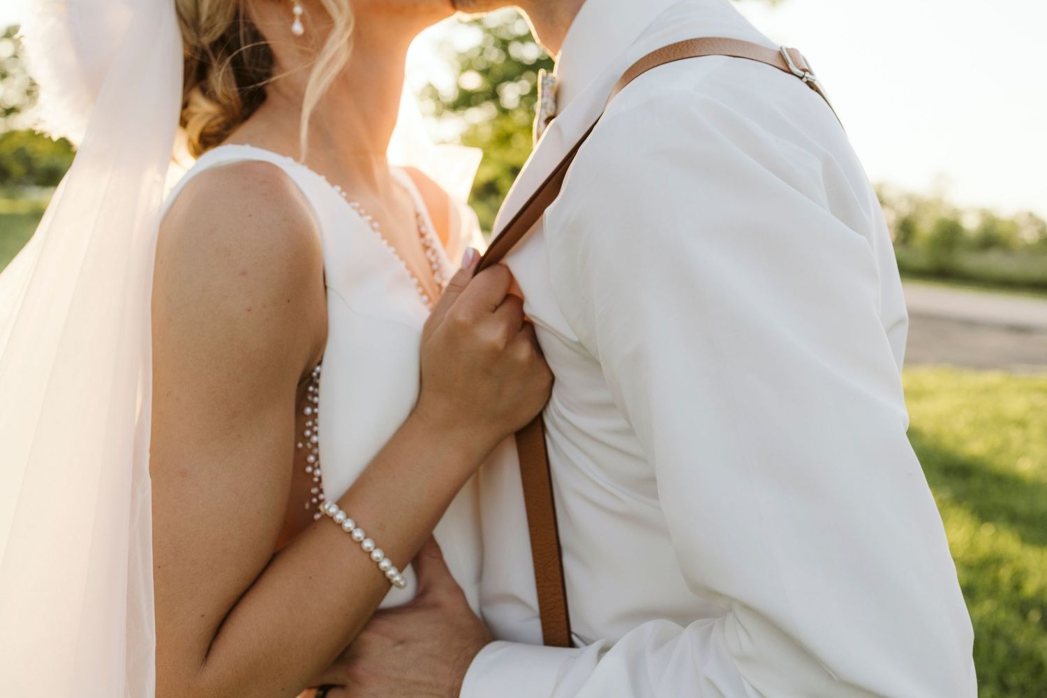 Elegant bride and groom share an intimate embrace in golden sunlight against a white garden pillar.