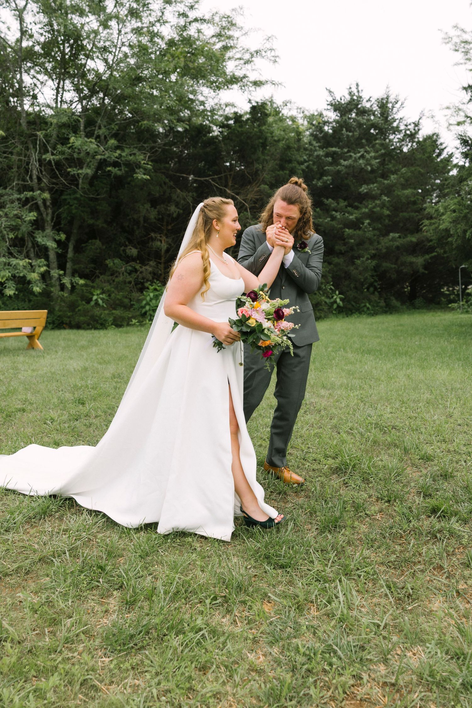 A couple shares an emotional moment on their wedding day outdoors, with the bride holding a beautiful floral bouquet.