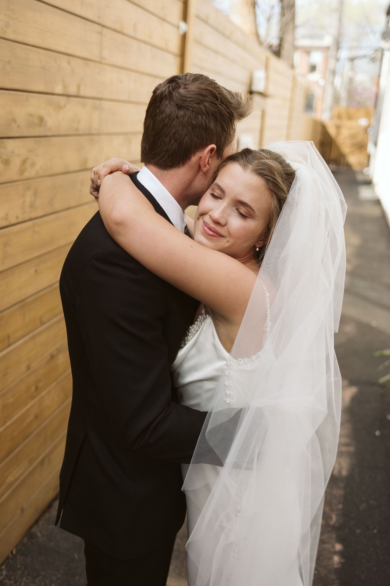 A bride and groom share an intimate embrace against a wooden wall during their wedding photos.