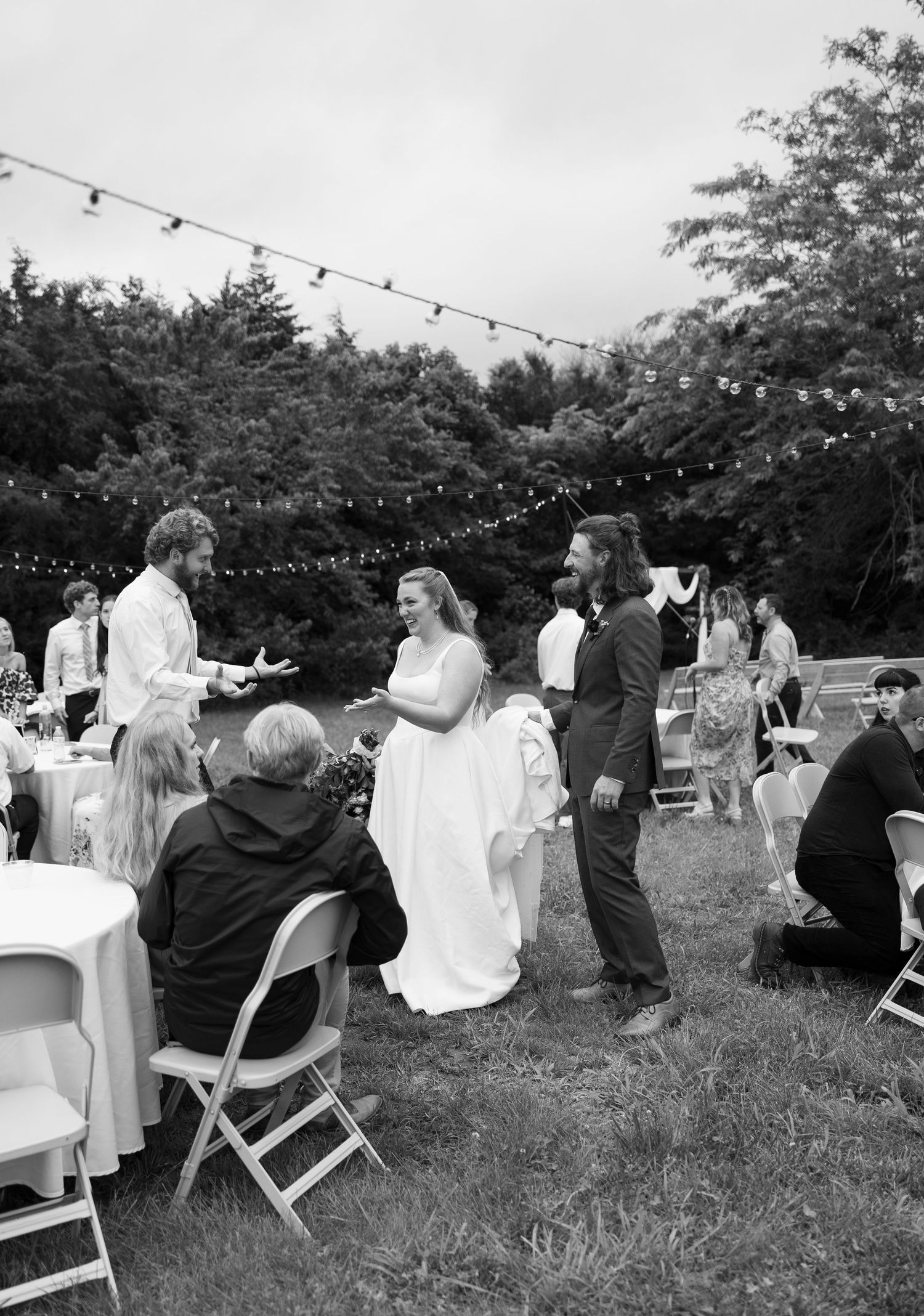 An outdoor wedding reception with string lights and guests dining at white tables.