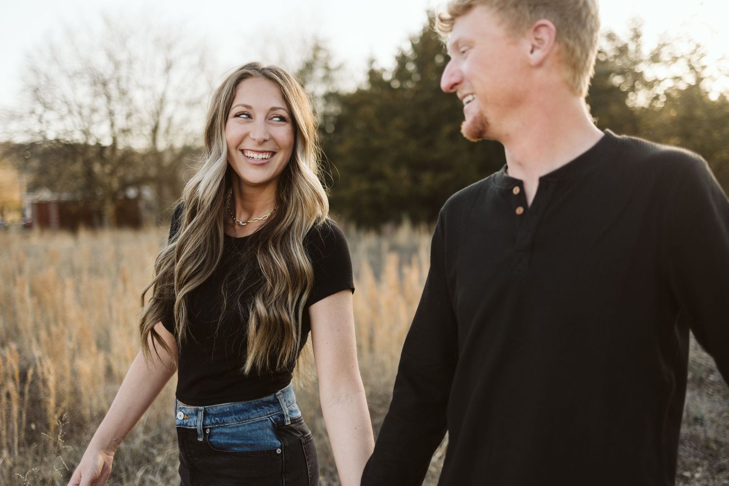 Couple laughing together in a golden field at sunset.