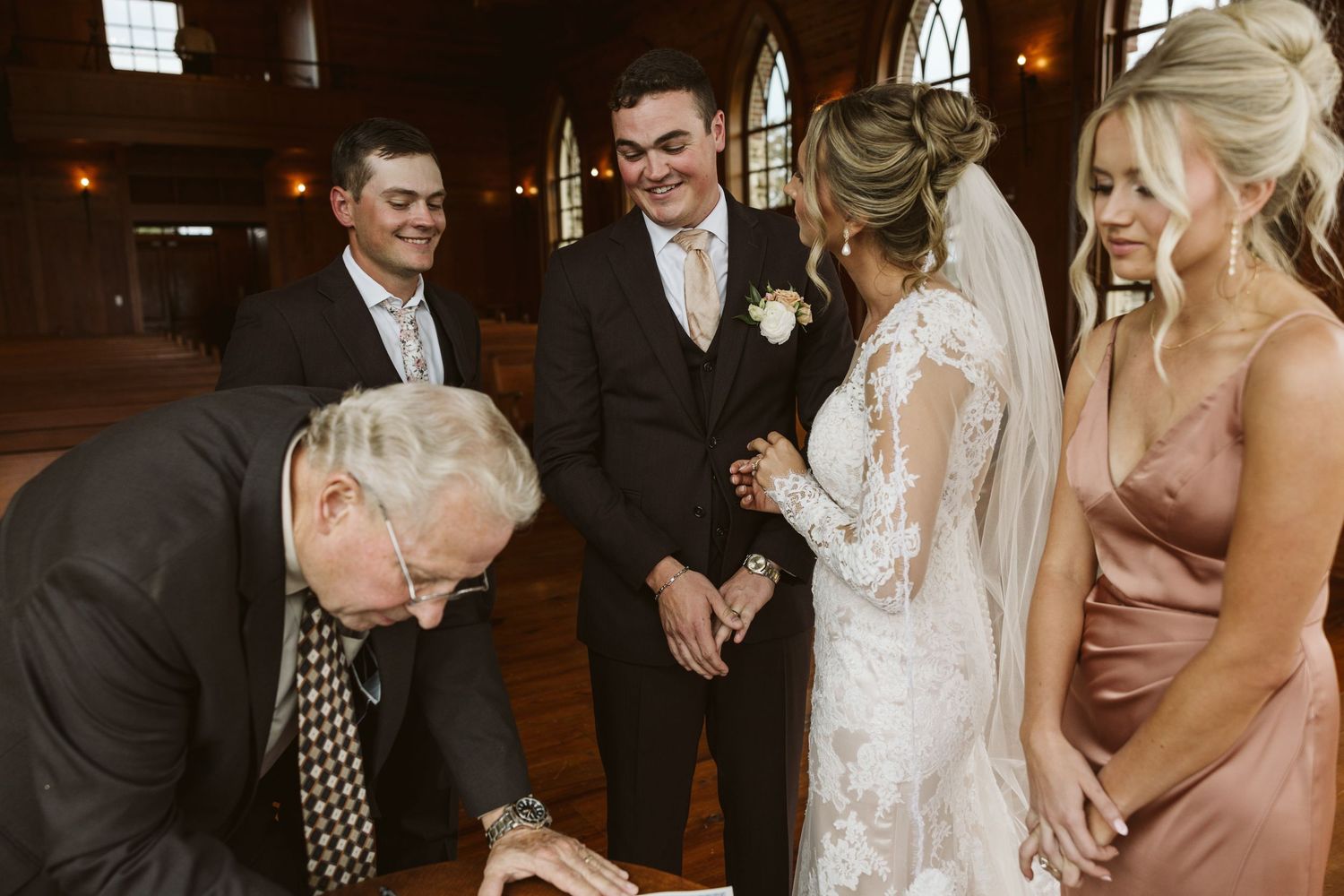 A wedding ceremony document signing moment indoors with a formal group gathered around.