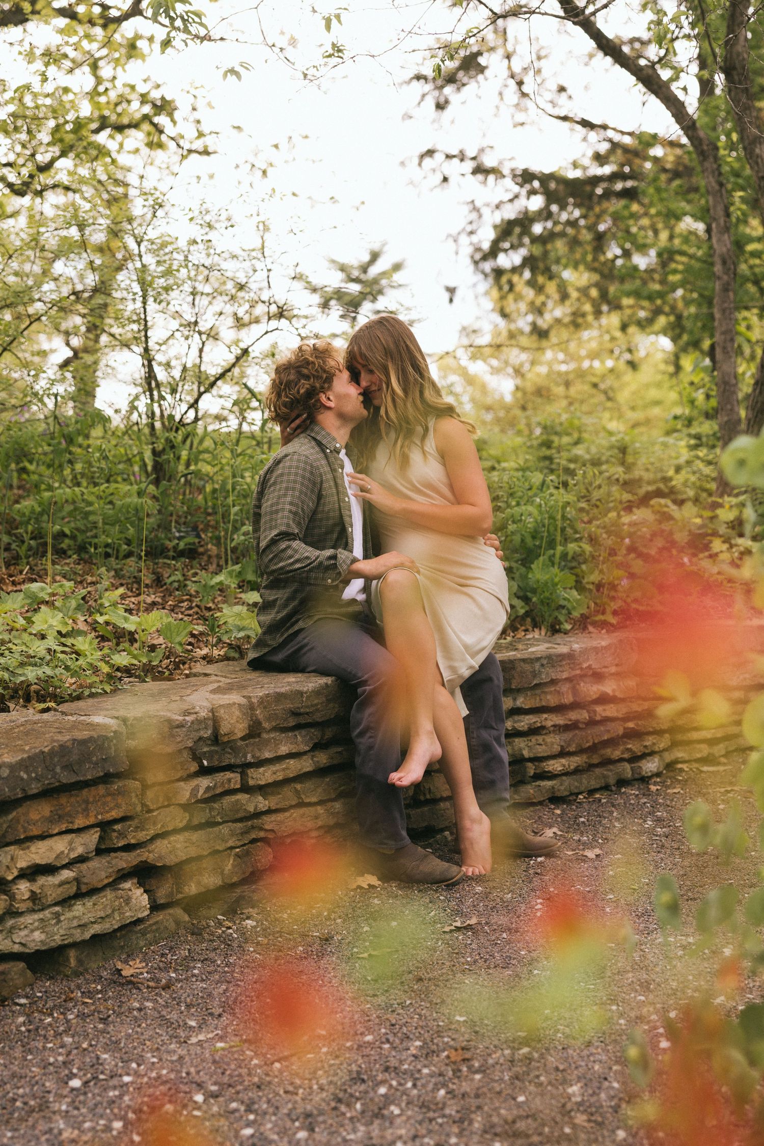 A romantic photoshoot on a stone wall path with natural sunlight and lens flares.