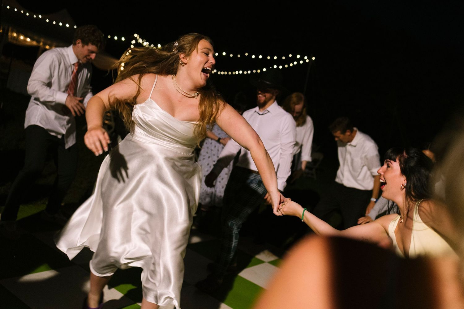 Dancing at a nighttime wedding reception with overhead string lights illuminating the energetic dance floor.