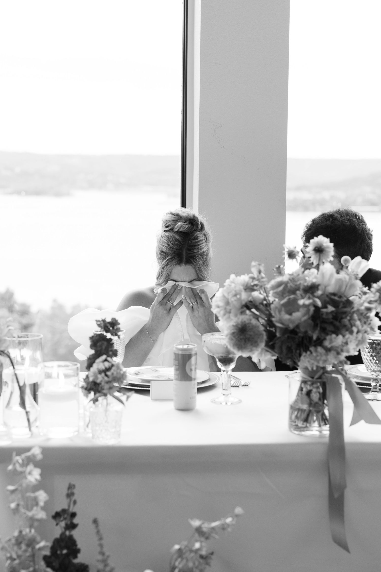 Black and white photo of floral centerpieces lined up along windowsill at wedding reception.