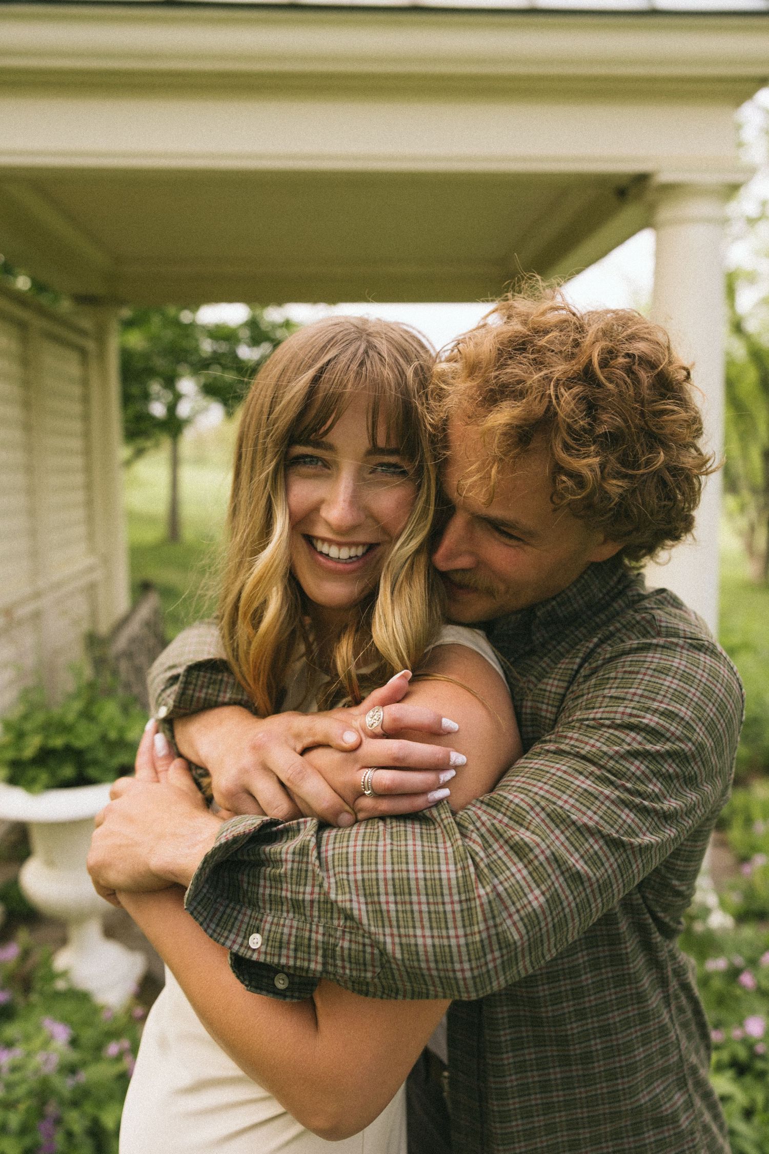 A sweet moment of laughter and embrace captured under a porch overhang during an outdoor photoshoot.