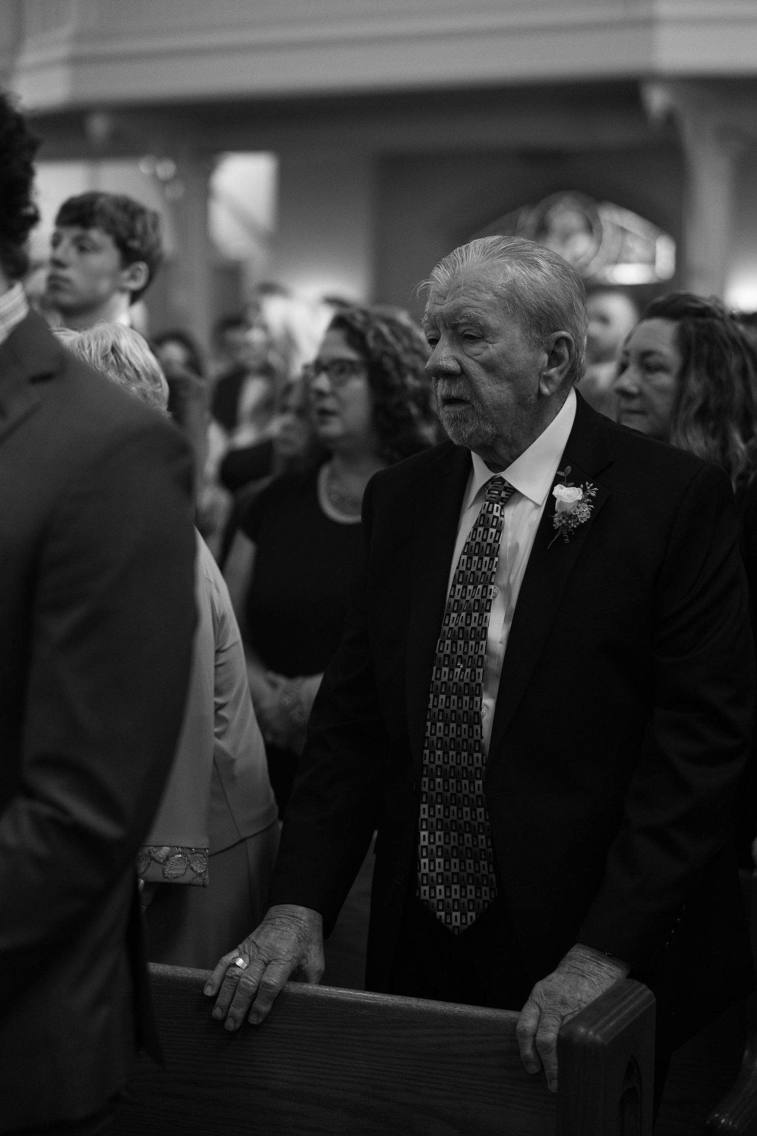 An elderly gentleman in a suit and tie stands attentively during a formal church ceremony.
