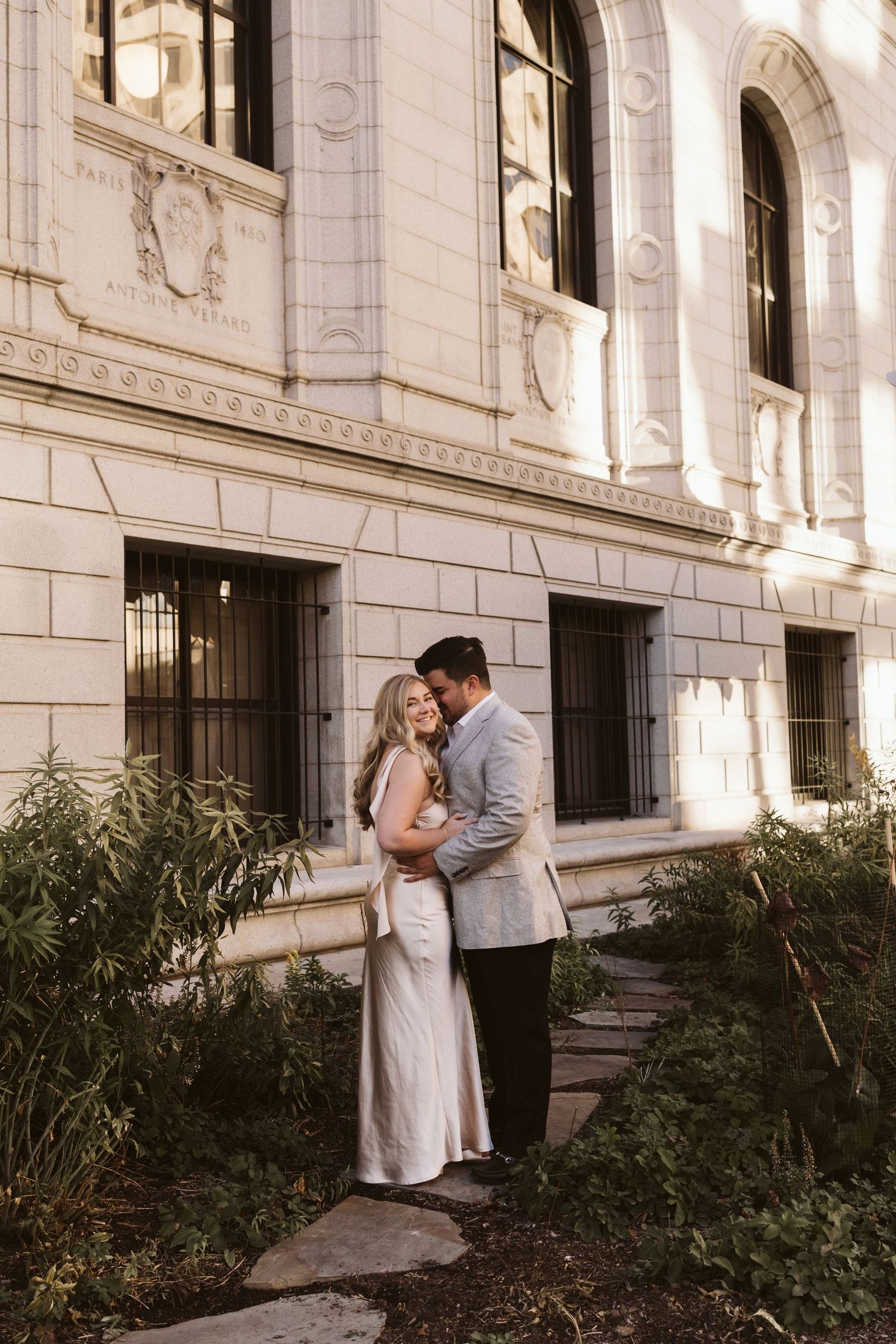 Intimate moment between couple against classic stone architecture and garden foliage.