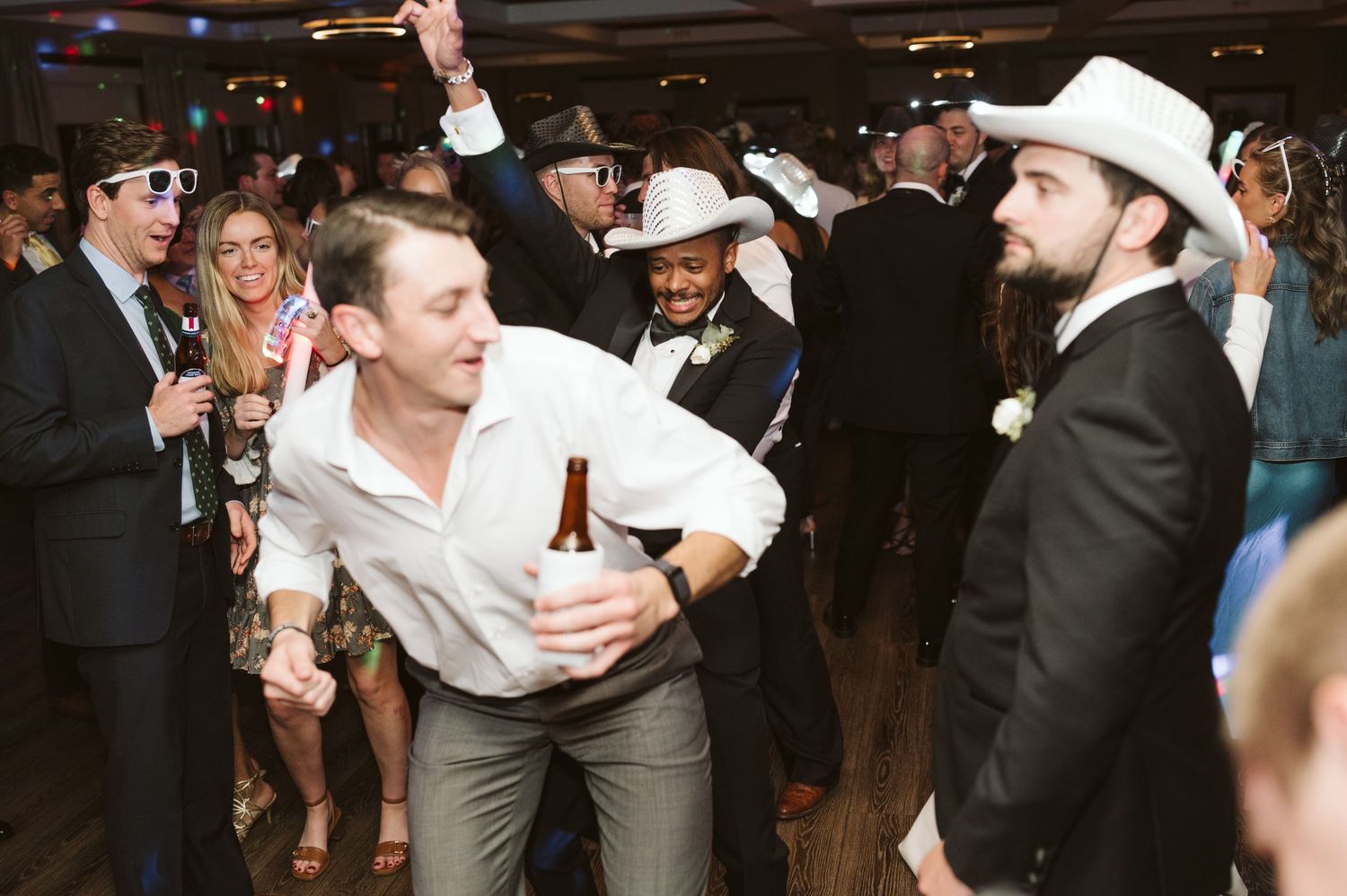 Wedding reception guests dance and celebrate with energetic movements on a crowded dance floor.