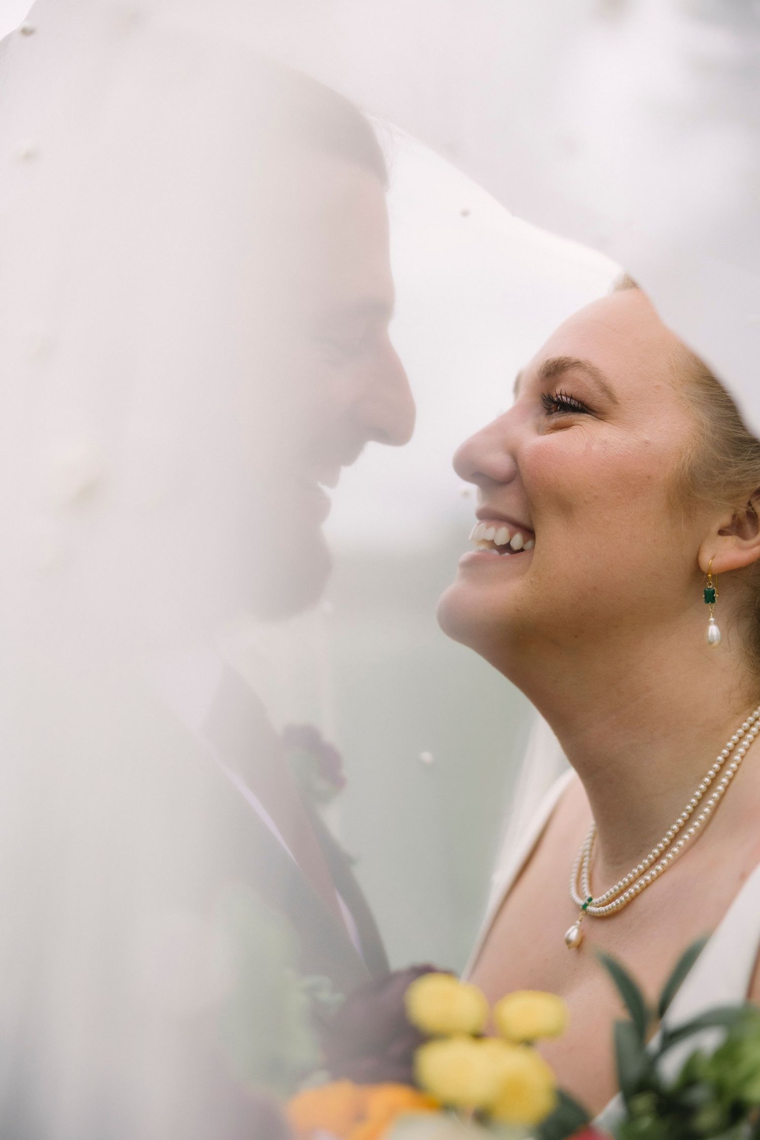 Close-up sequence of bride with pearl necklace laughing through sheer veil in soft lighting.
