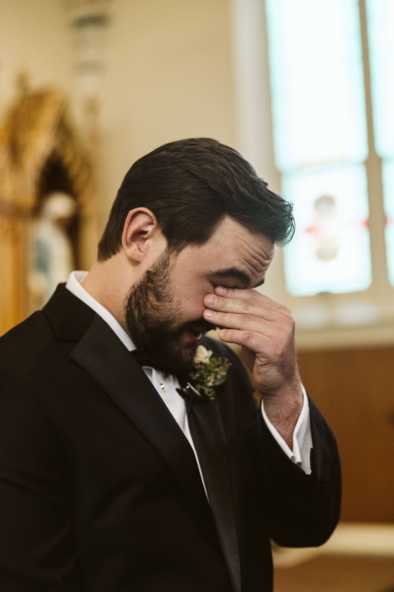 Emotional groom covering face during wedding ceremony in church setting.