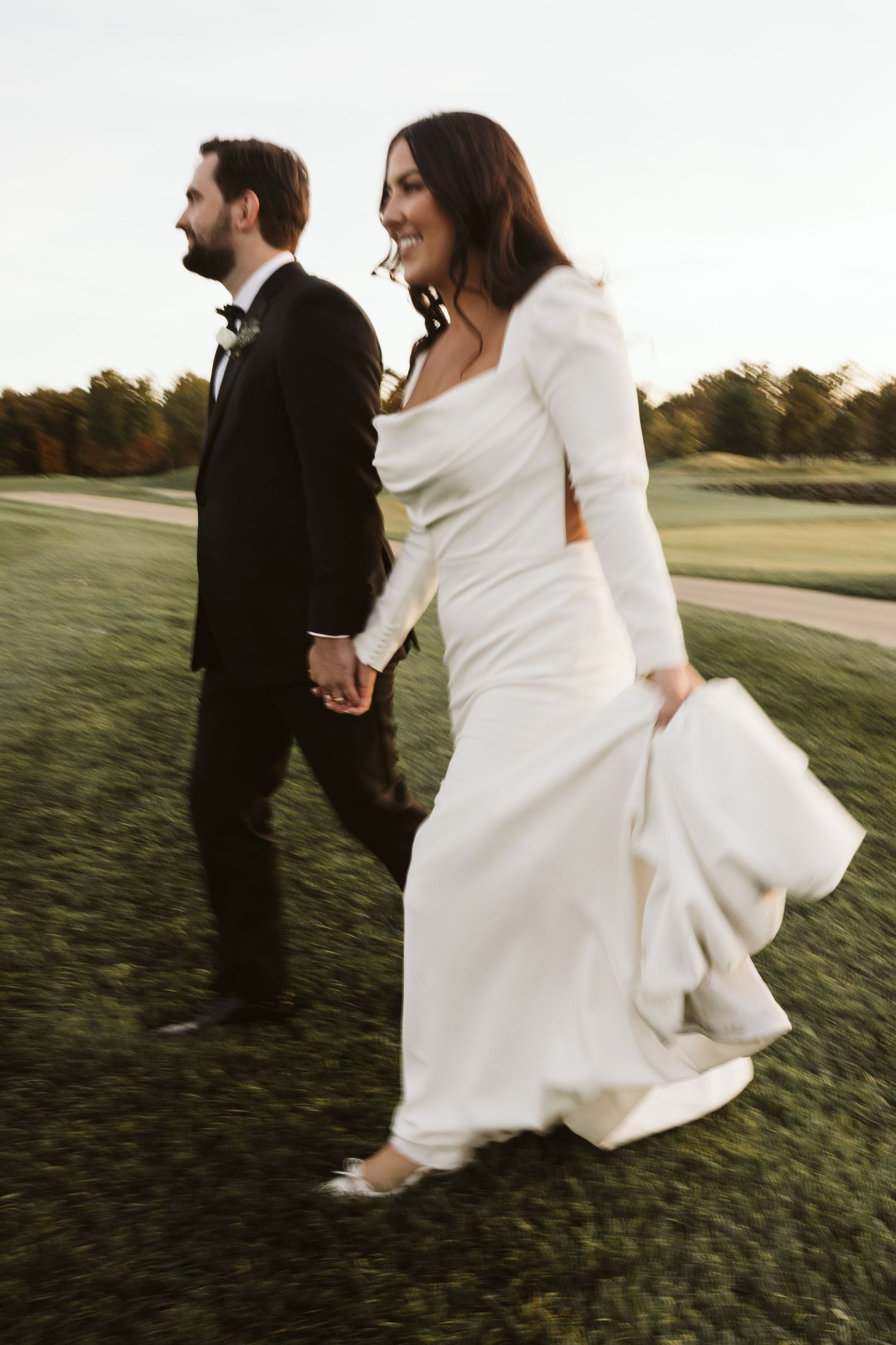 Newlyweds walking hand in hand across a sunset-lit golf course.