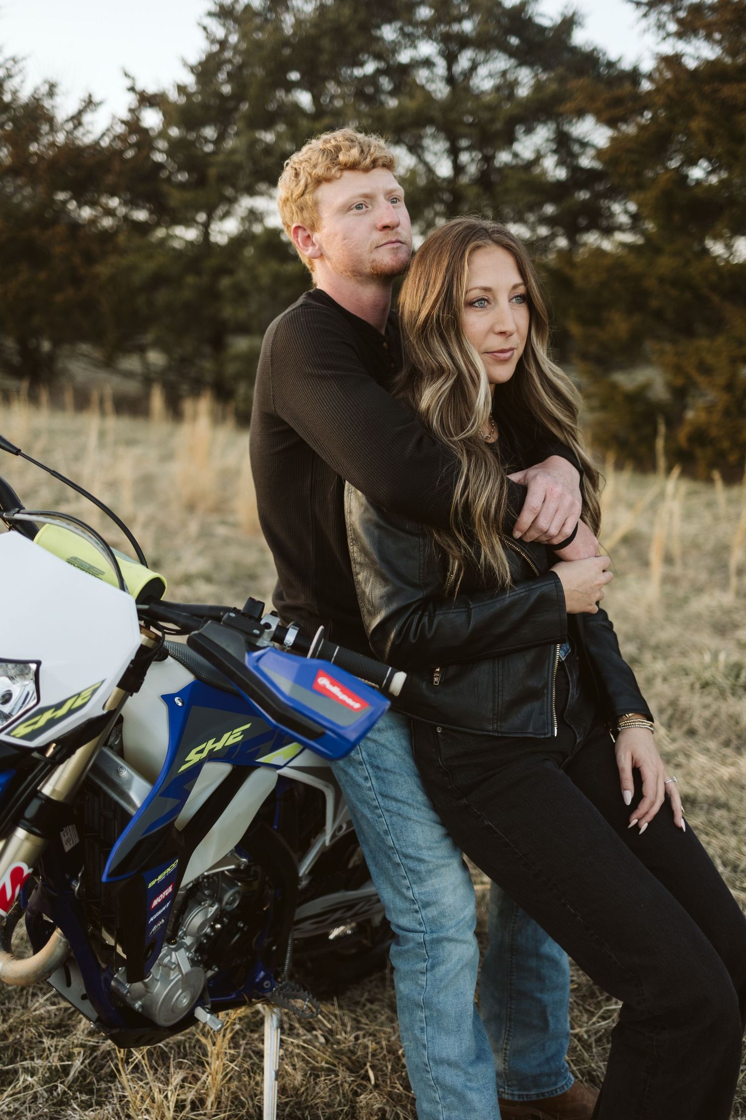 A romantic couple posing with a blue and white dirt bike in an autumn field.