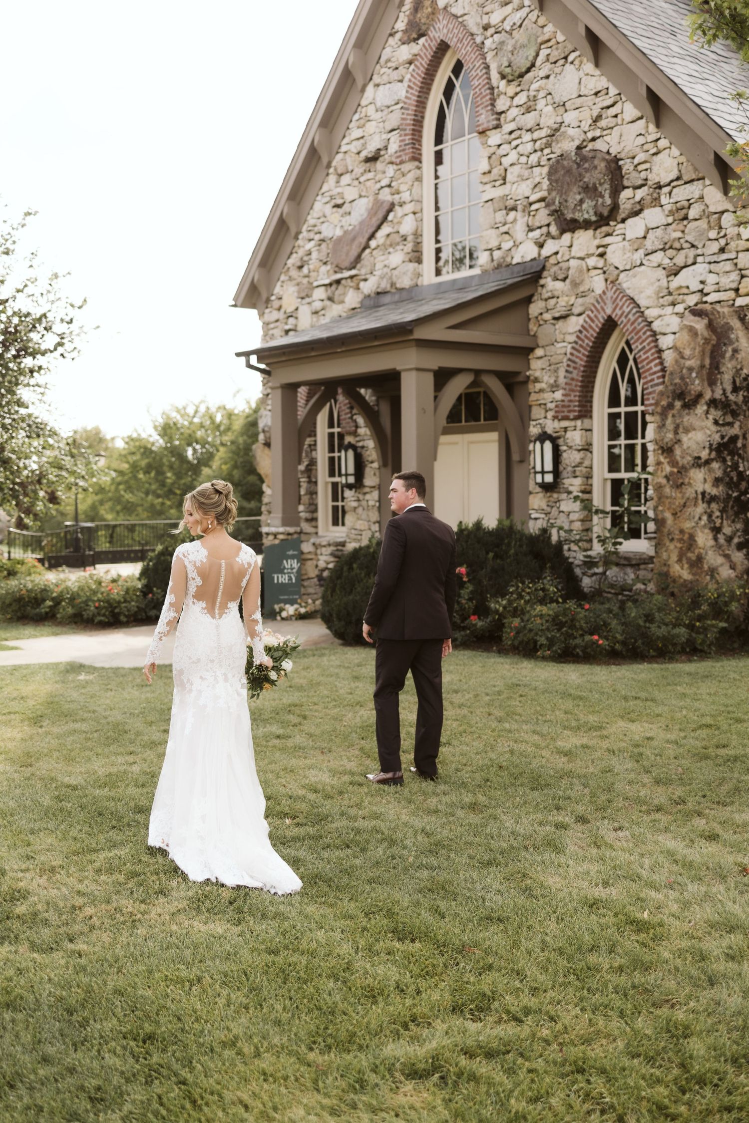 Bride and groom stand outside stone chapel with elegant architectural details.