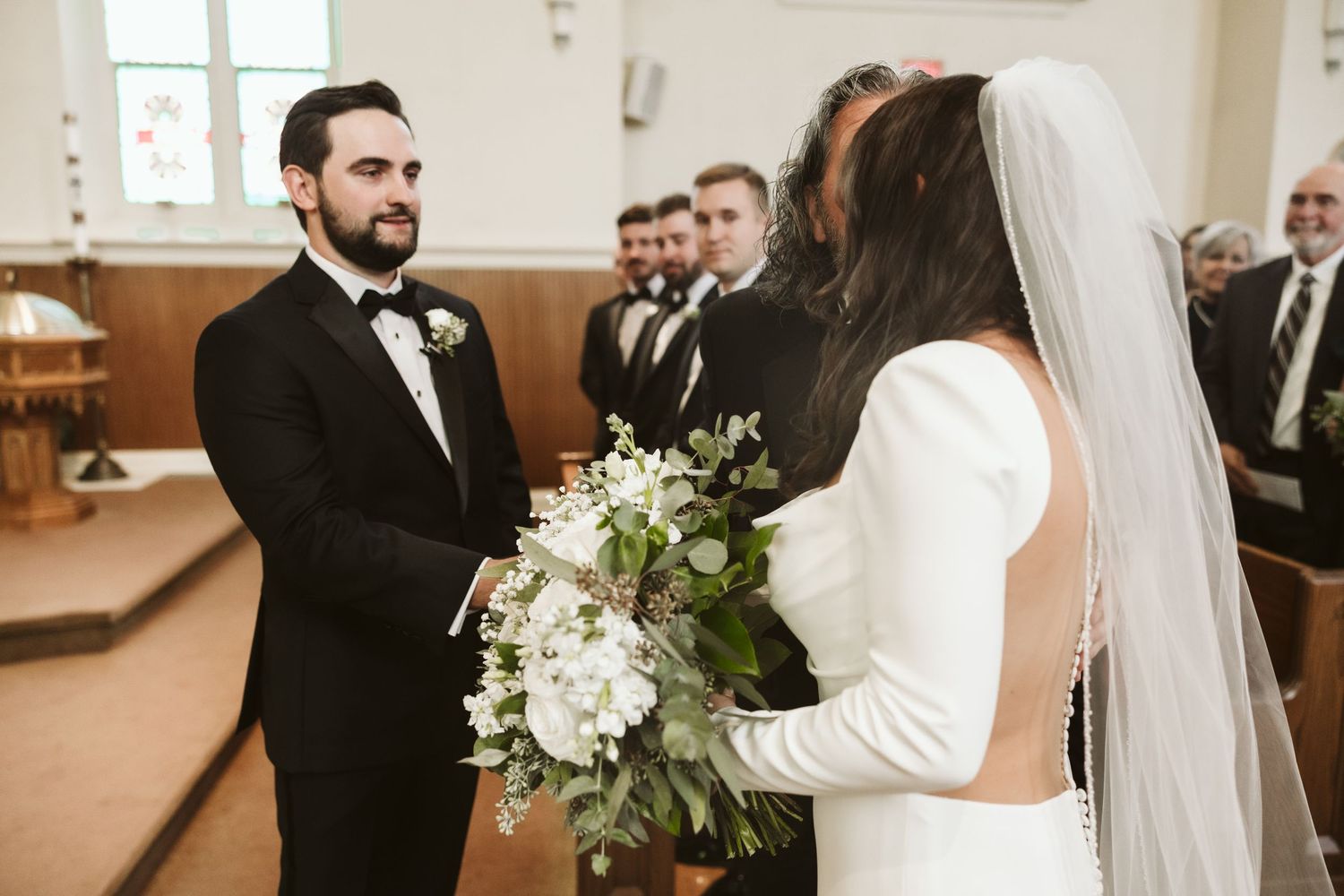 Side view of couple during wedding ceremony in church with stained glass windows.