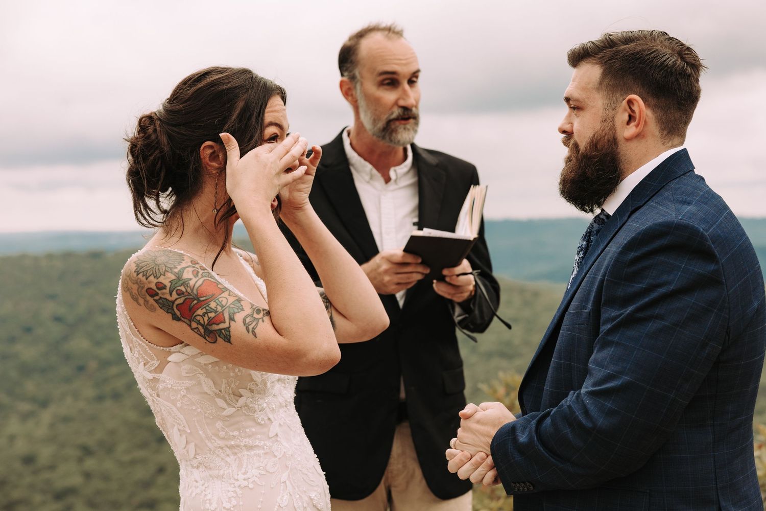Outdoor wedding ceremony with couple kissing and embracing while guests gather in a mountainous landscape setting.