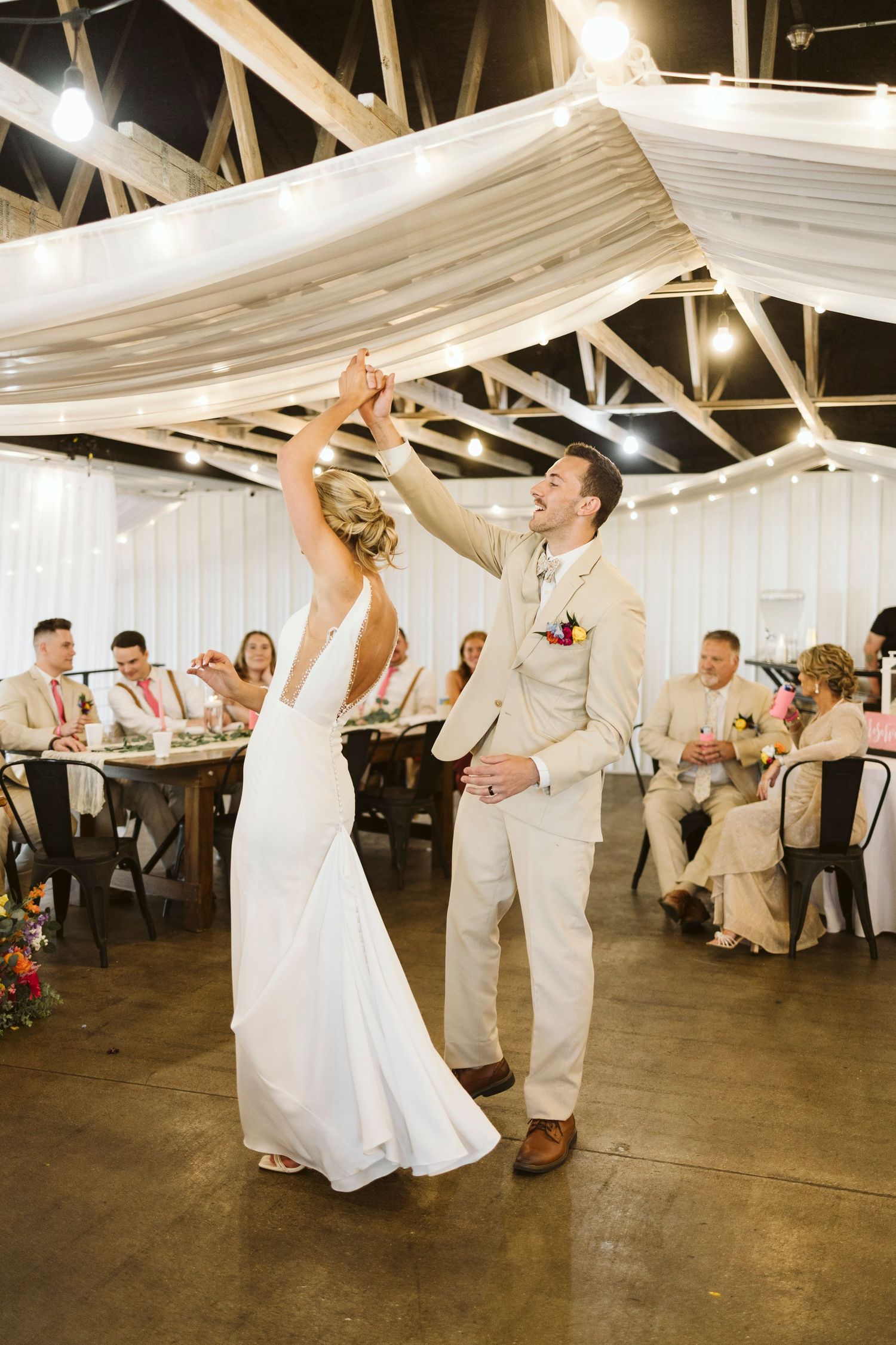 Lively wedding reception dancing scene with guests in white and khaki under draped ceiling.