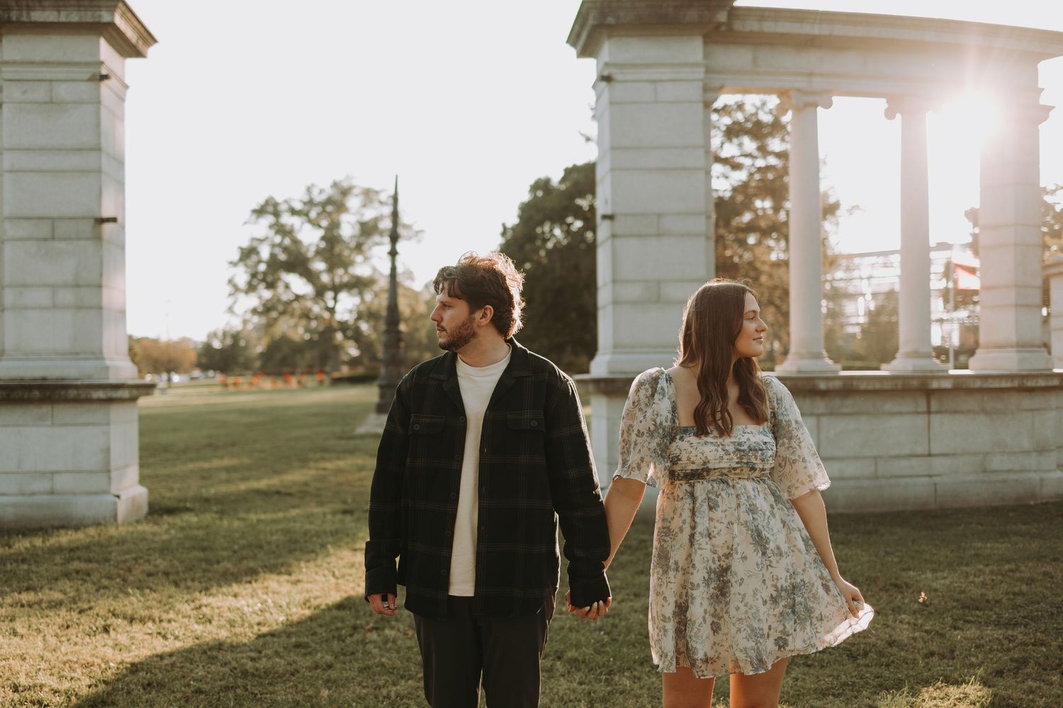 A couple walking together at sunset near white pillars, wearing casual romantic attire.