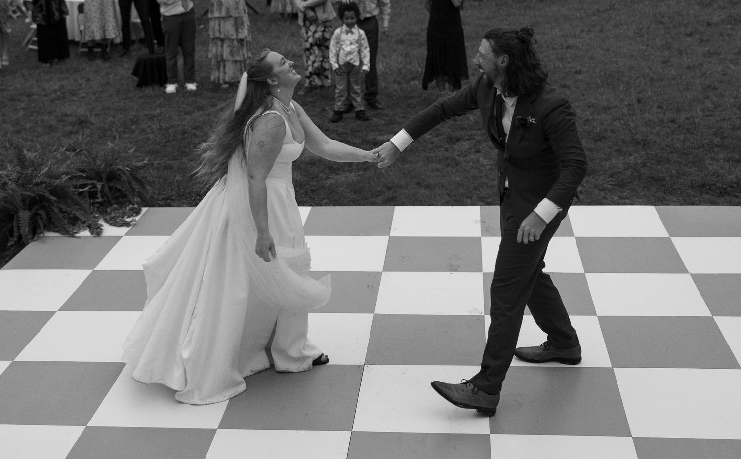 Wedding couples dance across an elegant outdoor checkerboard dance floor during a romantic celebration.