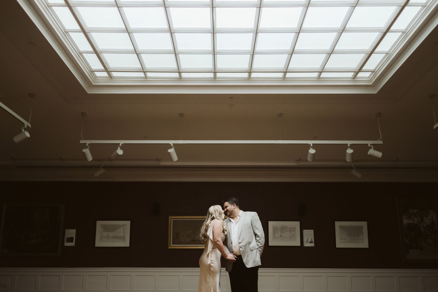 A couple standing beneath a skylight in an art gallery during their wedding.