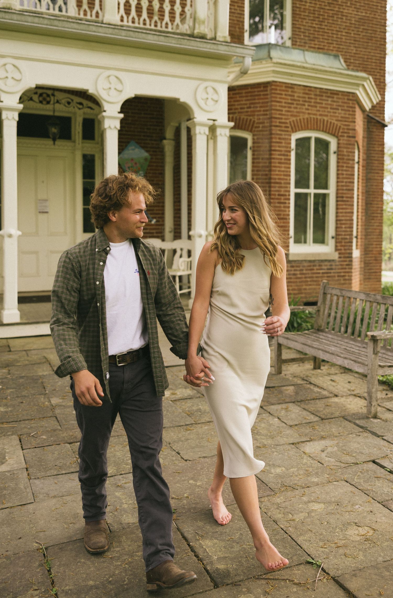A couple playfully interacts on a stone patio in front of a brick colonial style building.