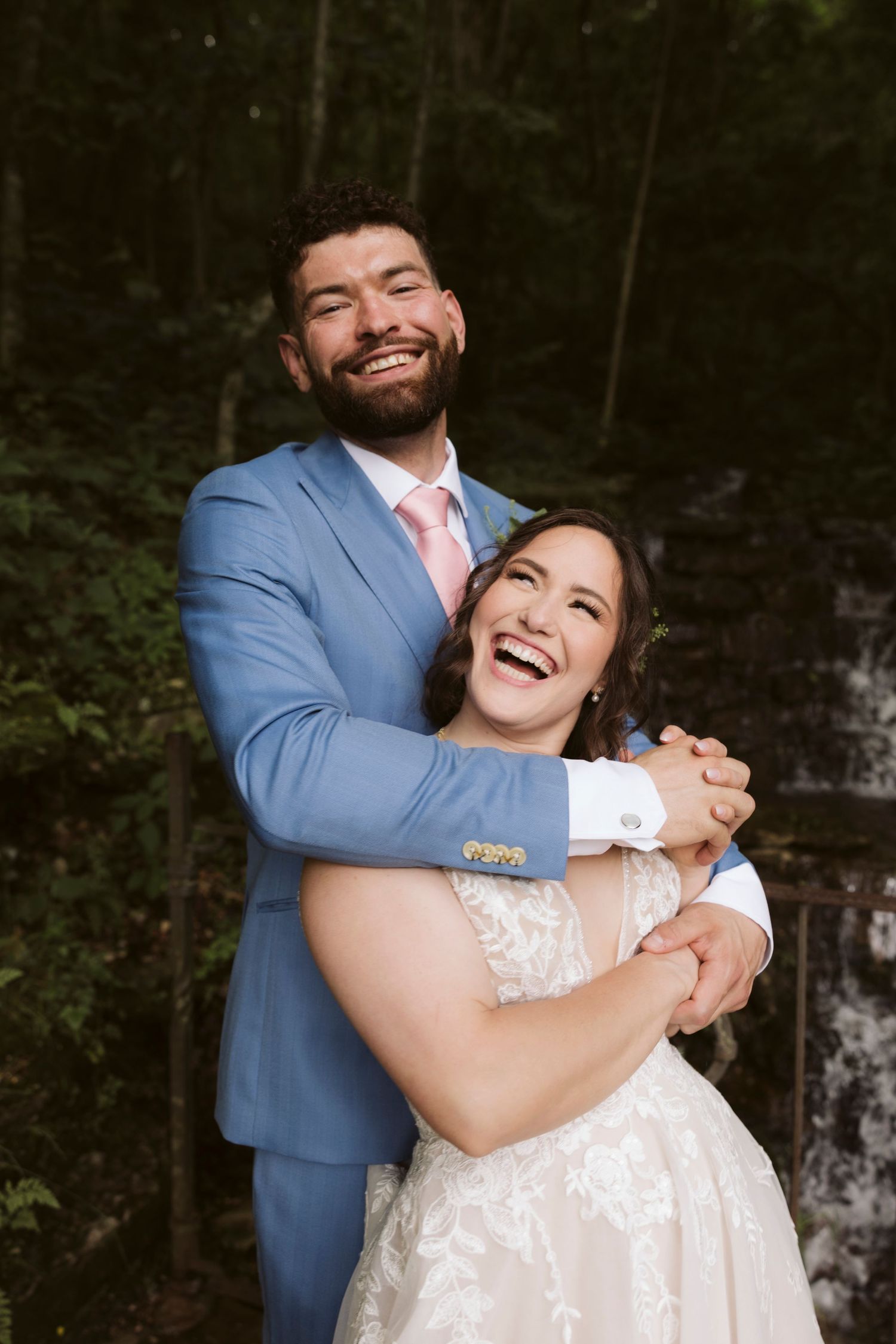 Couple shares joyful laughter during outdoor wedding photo session with natural scenery.