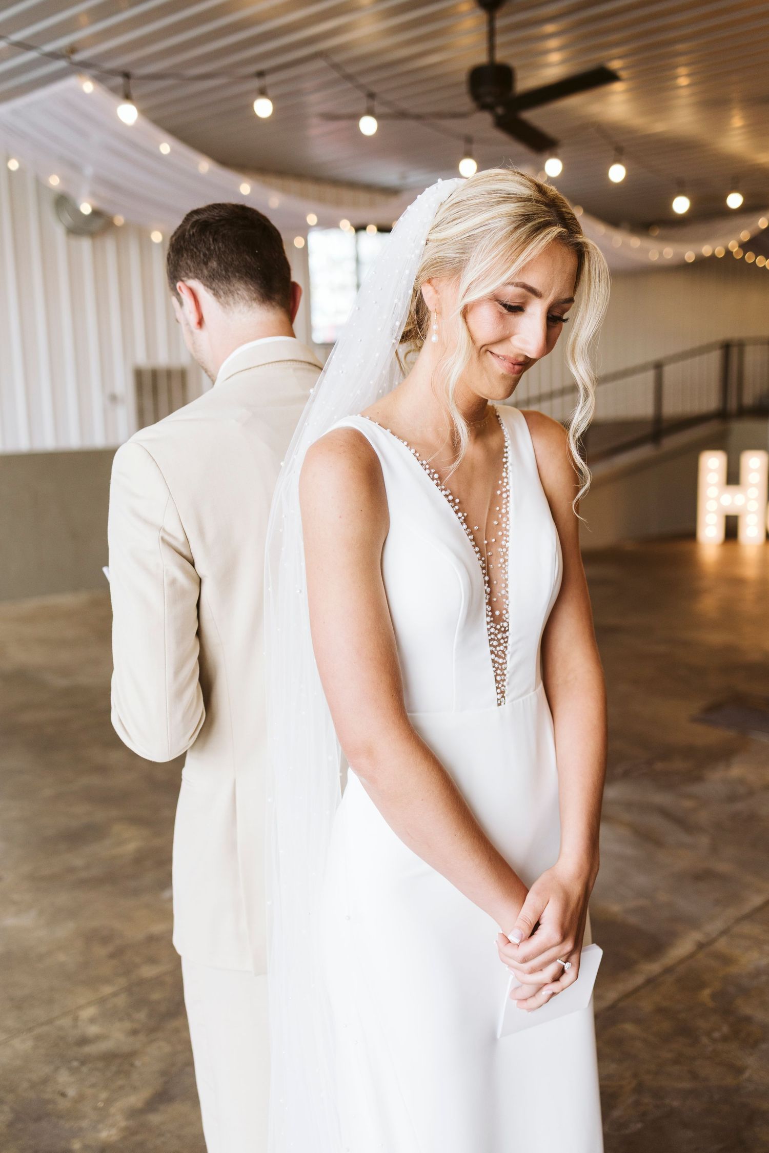 An intimate first look moment between a bride and groom in a modern industrial venue with string lights.