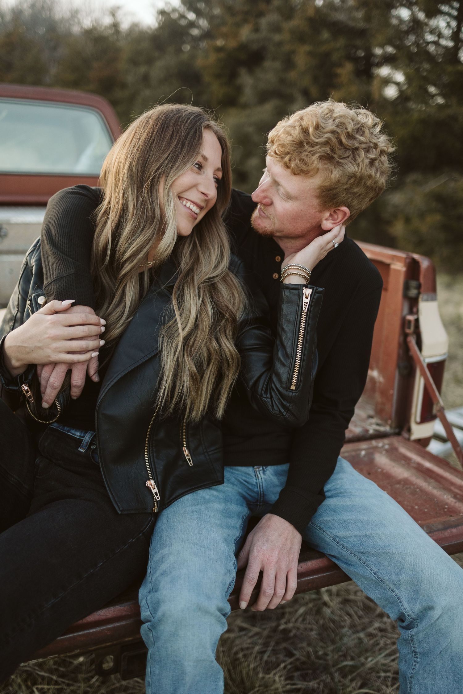 A couple sharing a laugh while sitting in the bed of a vintage red pickup truck.