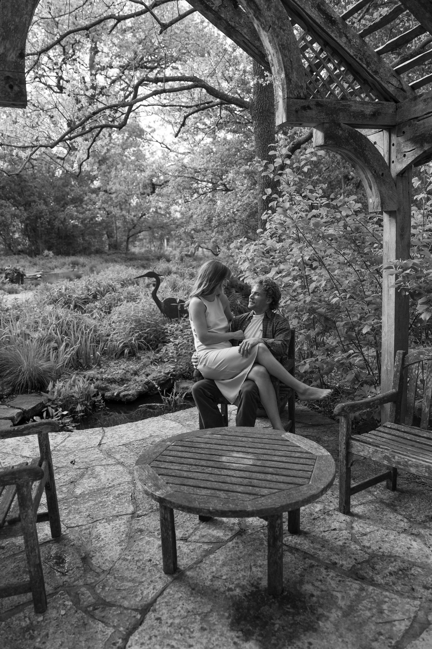 A romantic couple shares tender moments together on a wooden bench in a garden pergola.