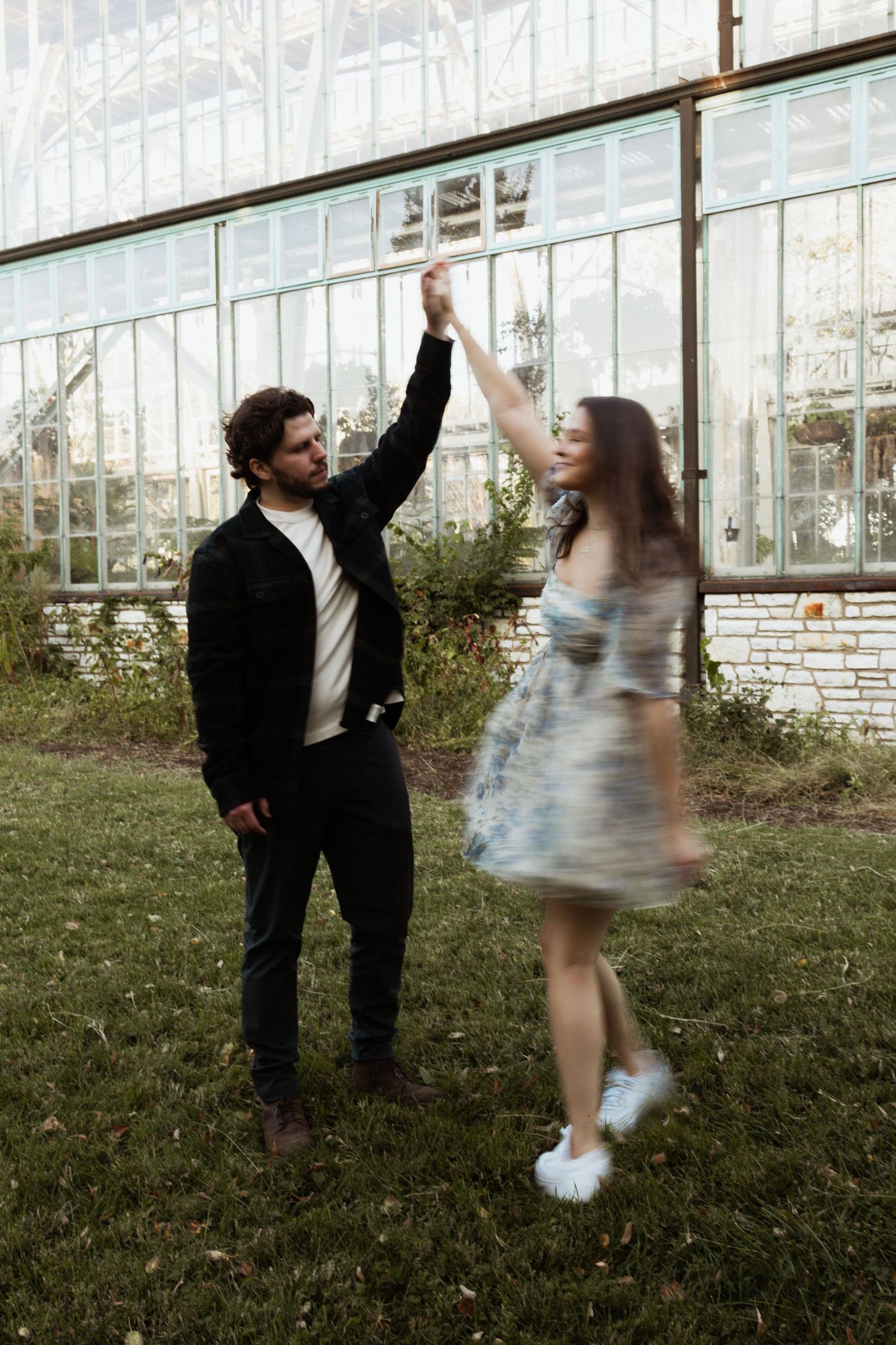 A playful dancing scene in front of a greenhouse with raised arms.