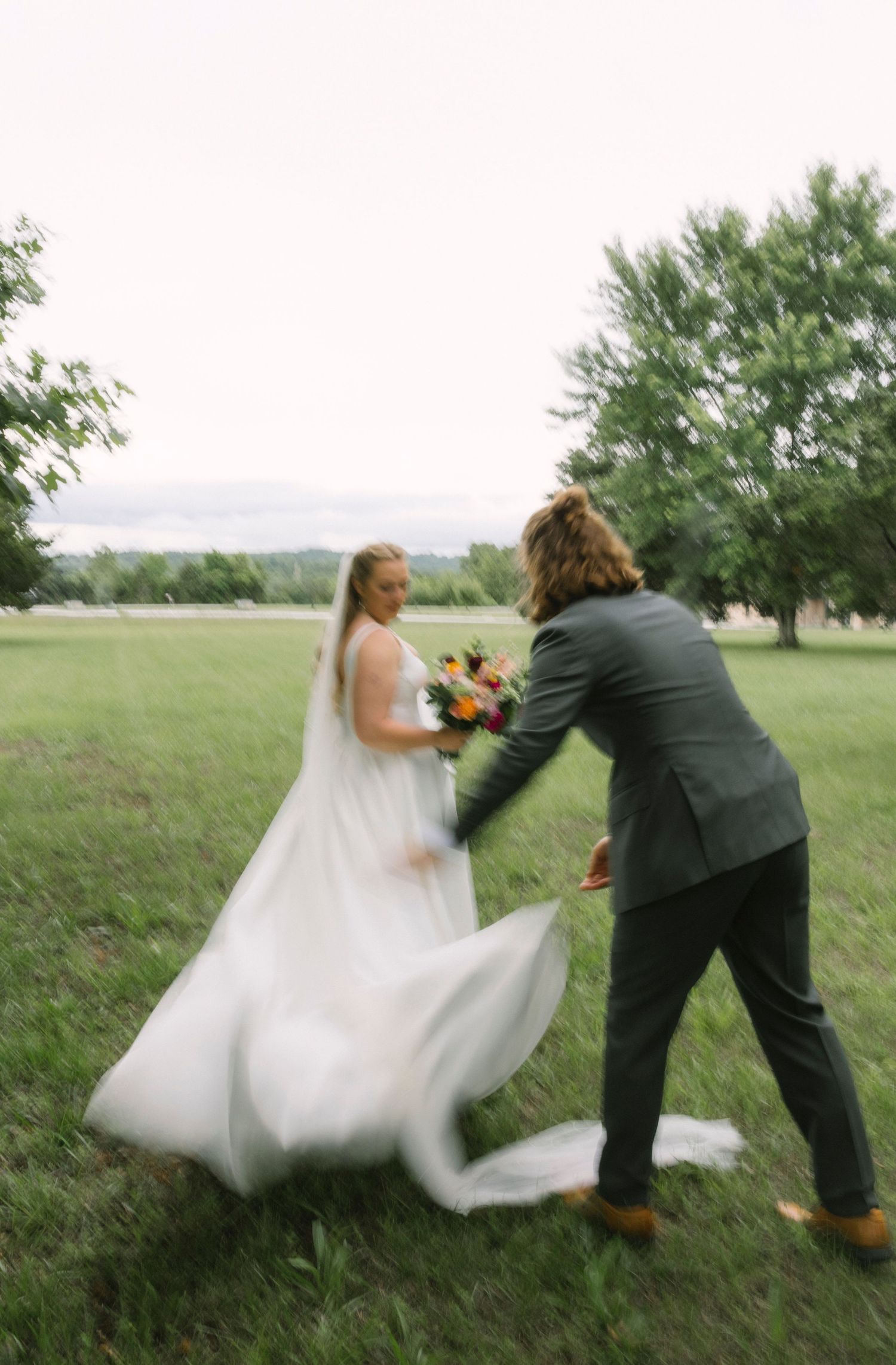 Sequence of playful wedding couple twirling in a grassy field with the bride's dress flowing in the breeze.
