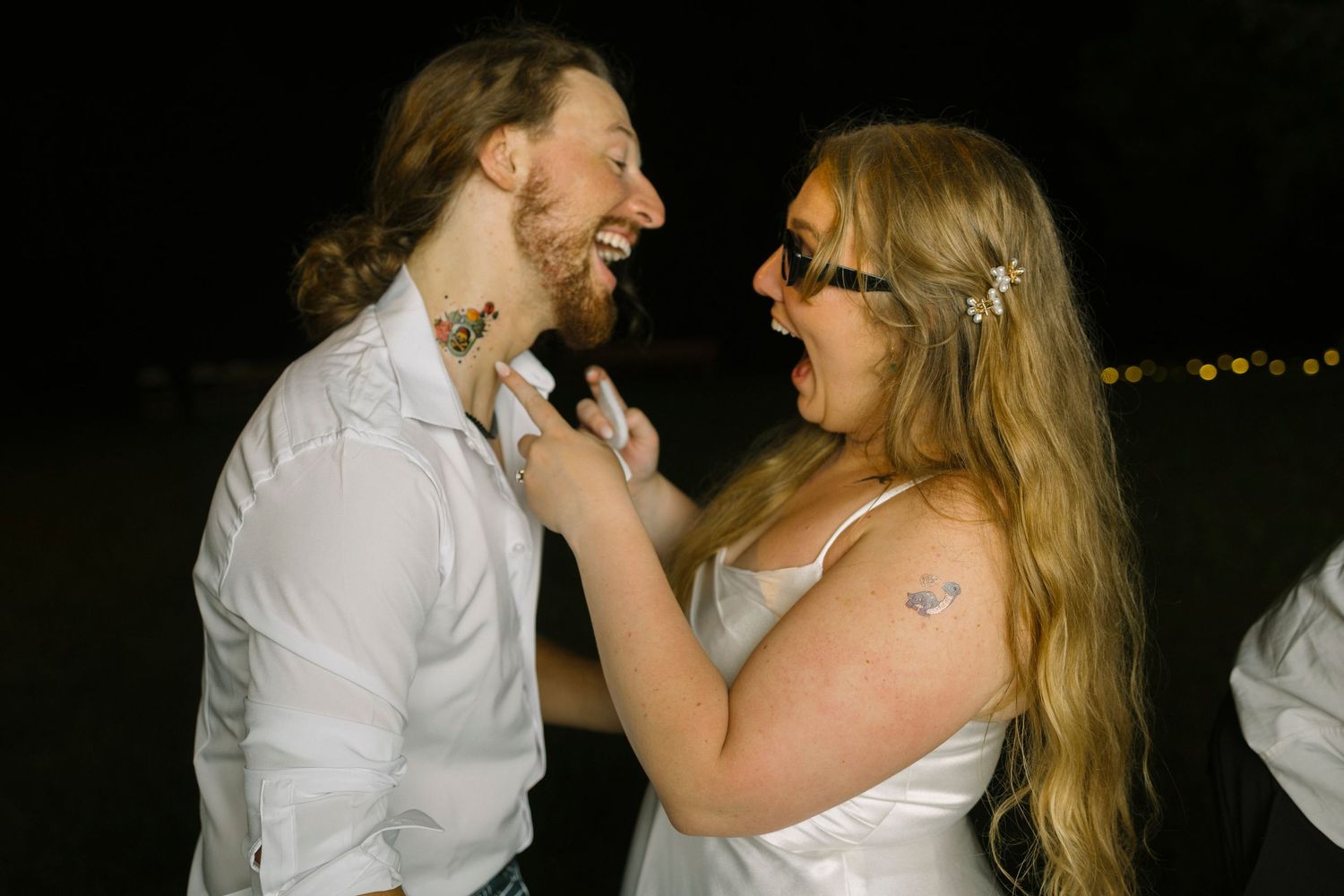 A couple shares an intimate moment of laughter while dancing together at a nighttime wedding reception.