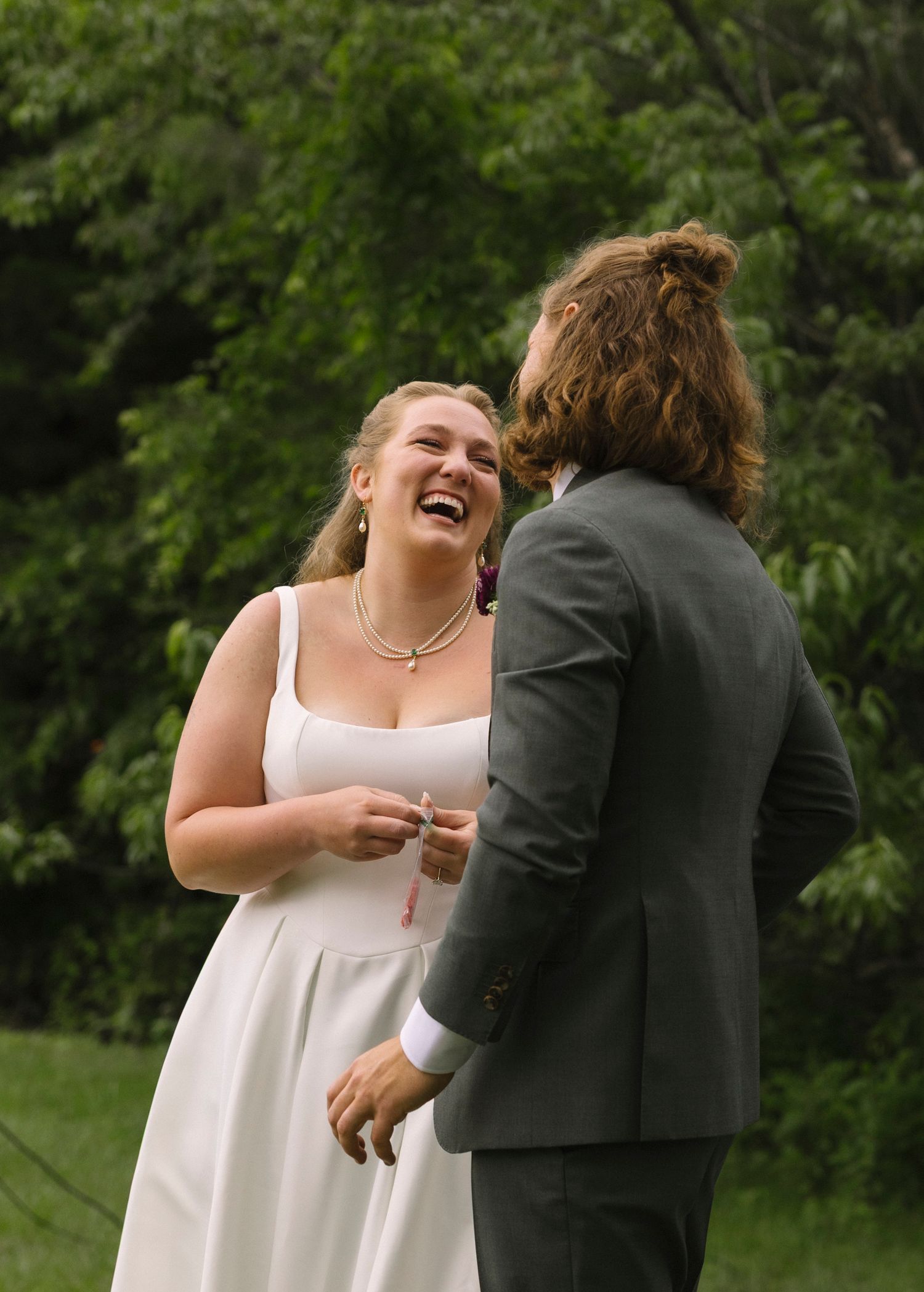 Two people share a candid joyful moment together during an outdoor wedding ceremony against a green background.
