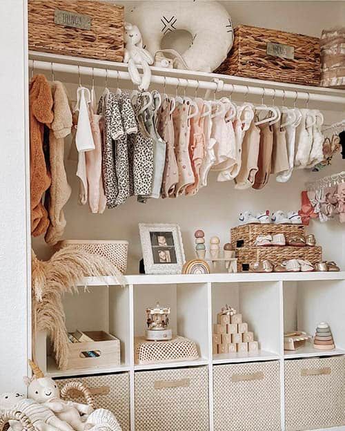 Organized nursery closet with blush and neutral toned baby clothes and storage bins.