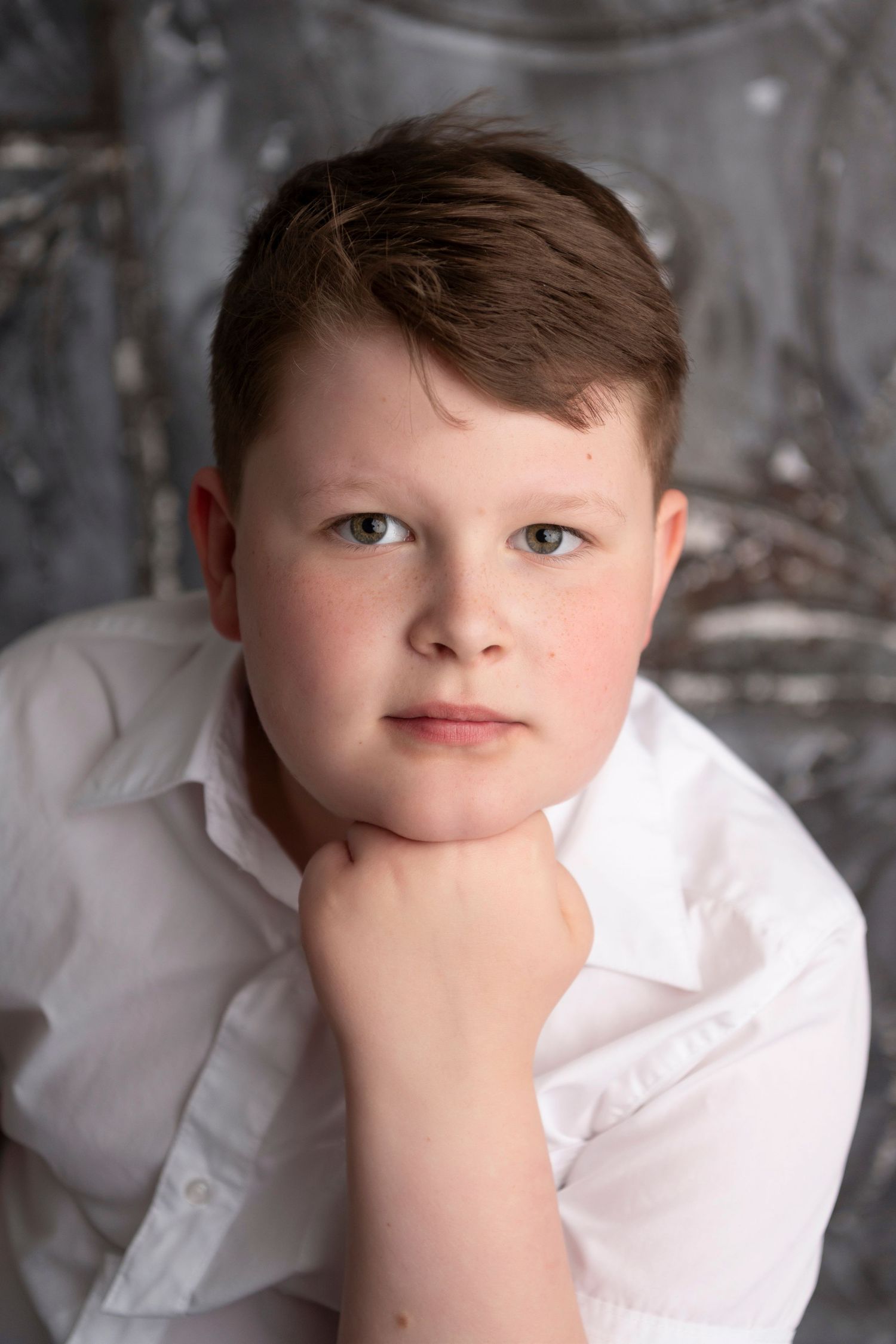 A studio portrait of a youth in a white dress shirt against a textured gray background.