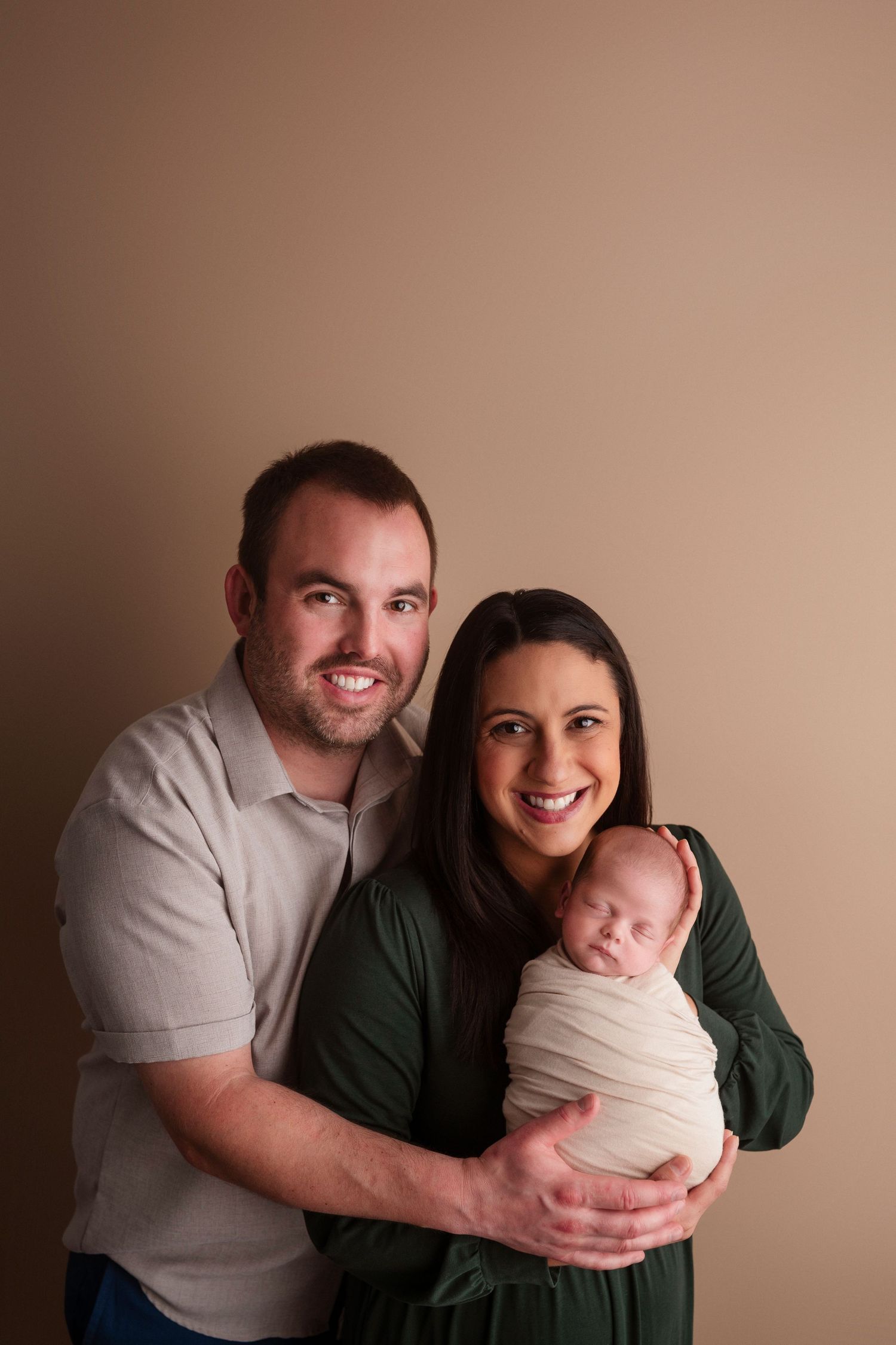 Parents in casual attire share tender moments with their newborn baby in a minimalist portrait studio series.