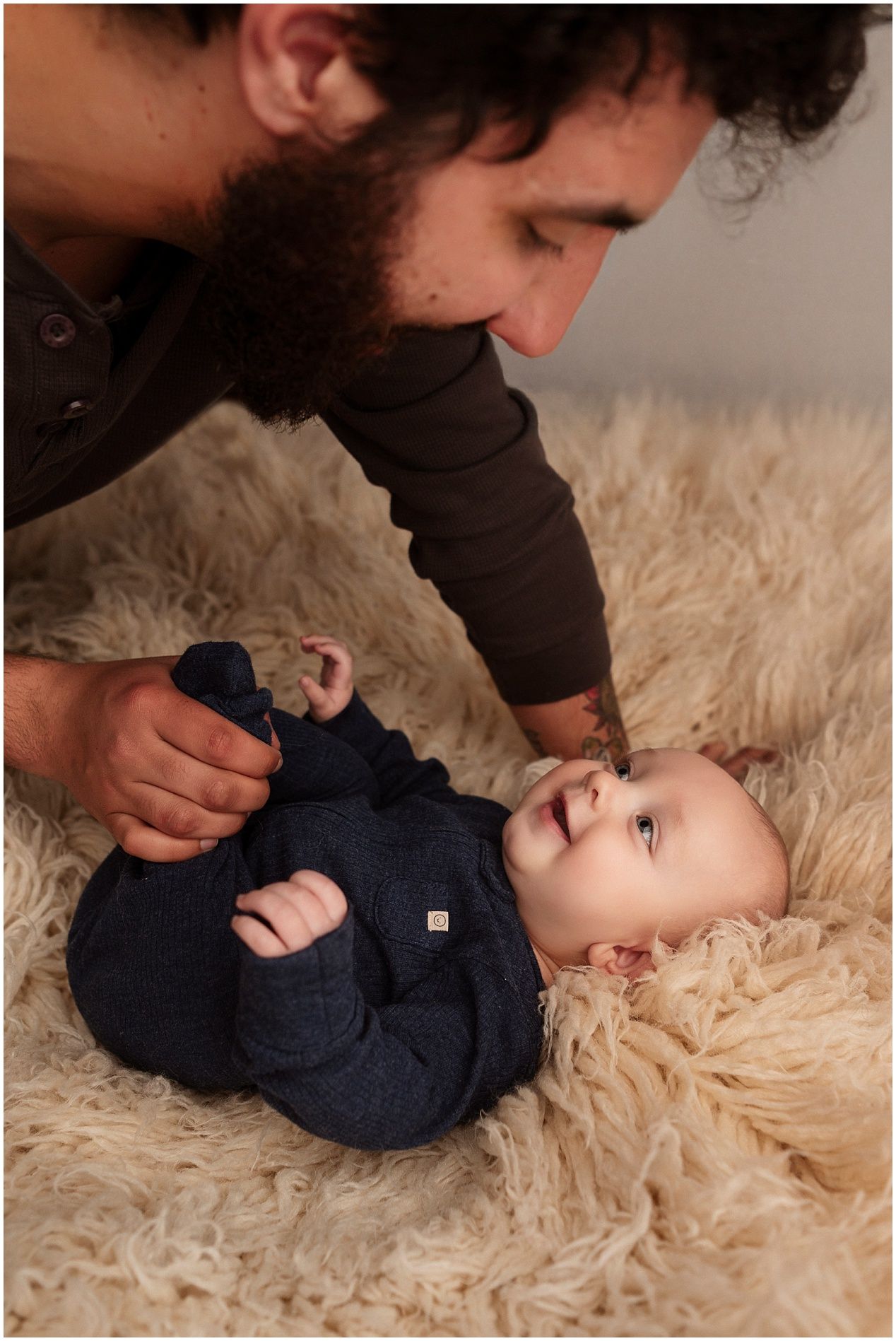 Parent playing with baby wearing navy outfit on soft beige rug during lifestyle photoshoot.