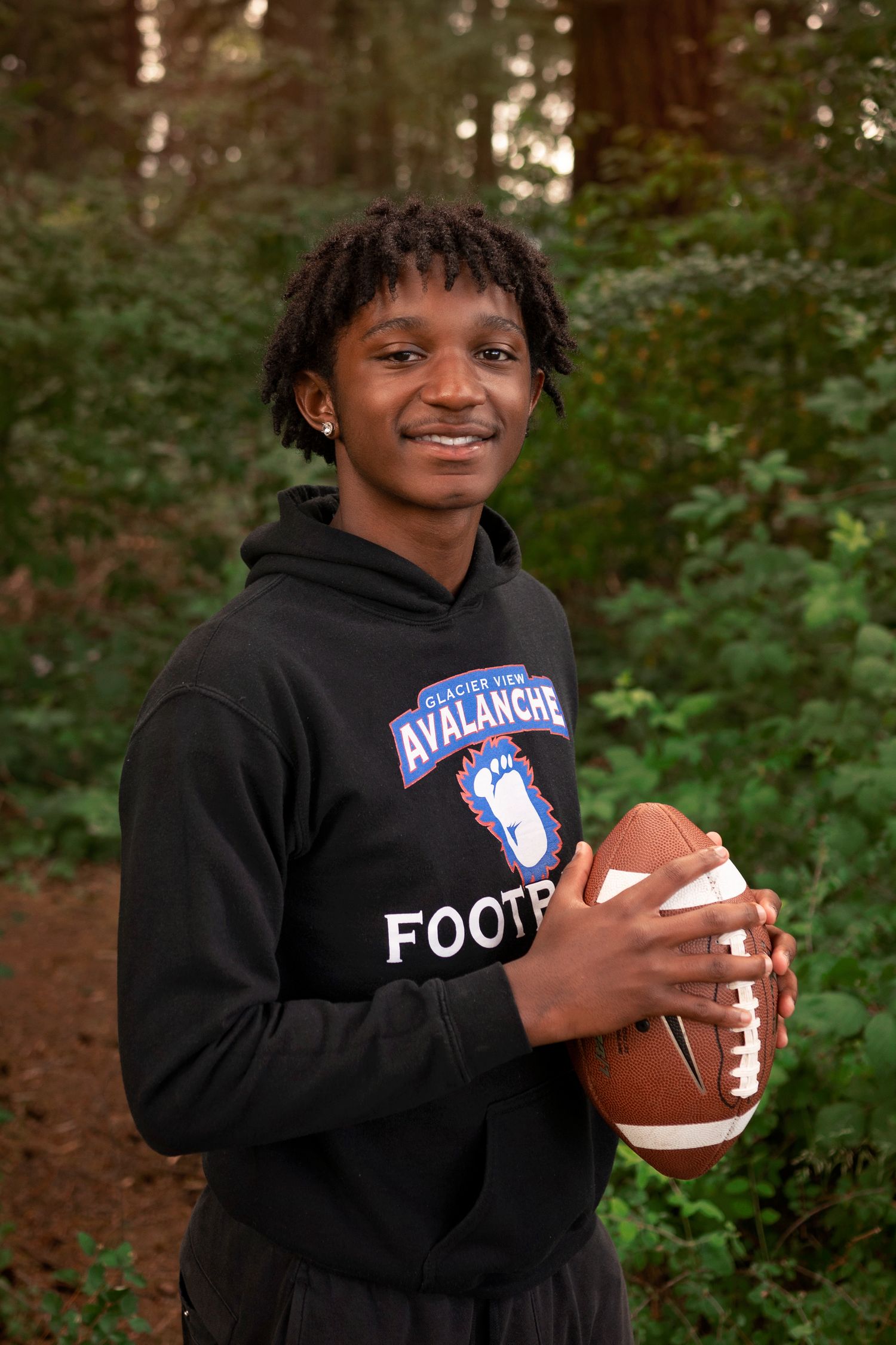 Young athlete in black Avalanche Football hoodie holding football outdoors.