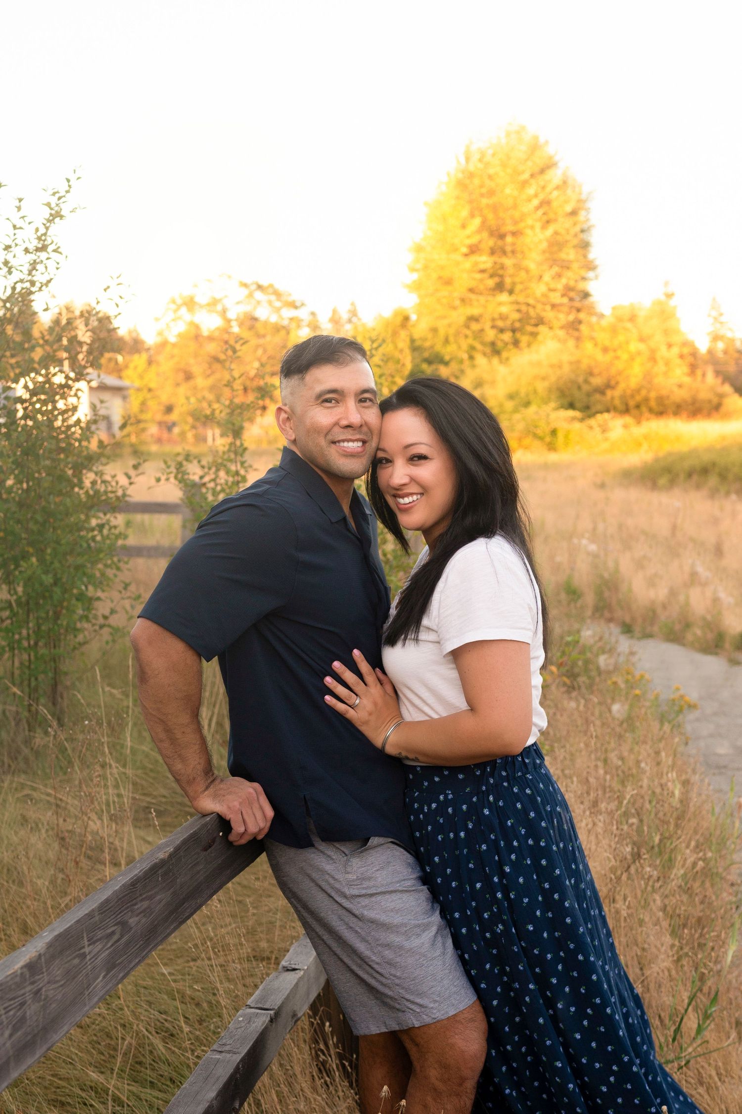 Couple embracing and smiling on wooden boardwalk during golden sunset.