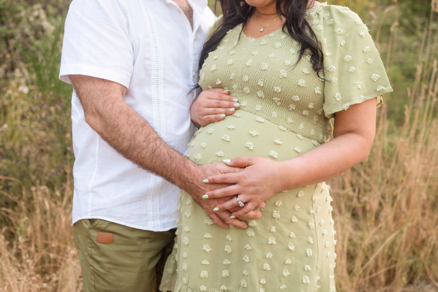 Maternity photo of couple's hands on pregnant belly wearing white and sage green outfits.