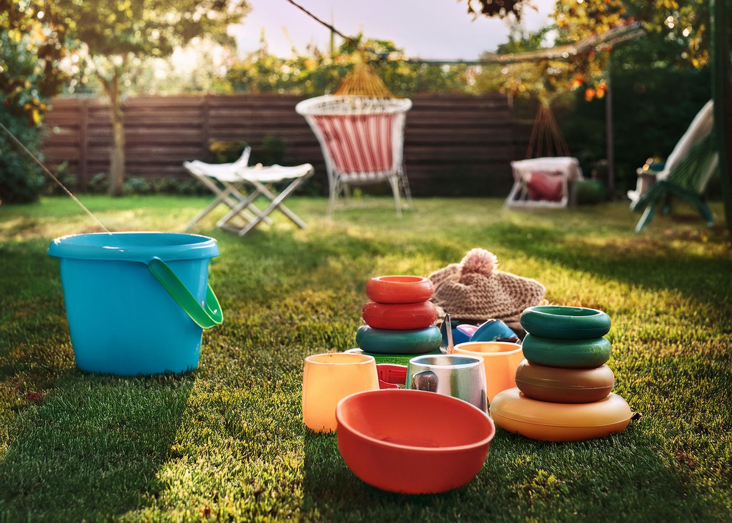 Colorful plastic bowls and plates scattered on grass in warm sunlit backyard during evening golden hour.