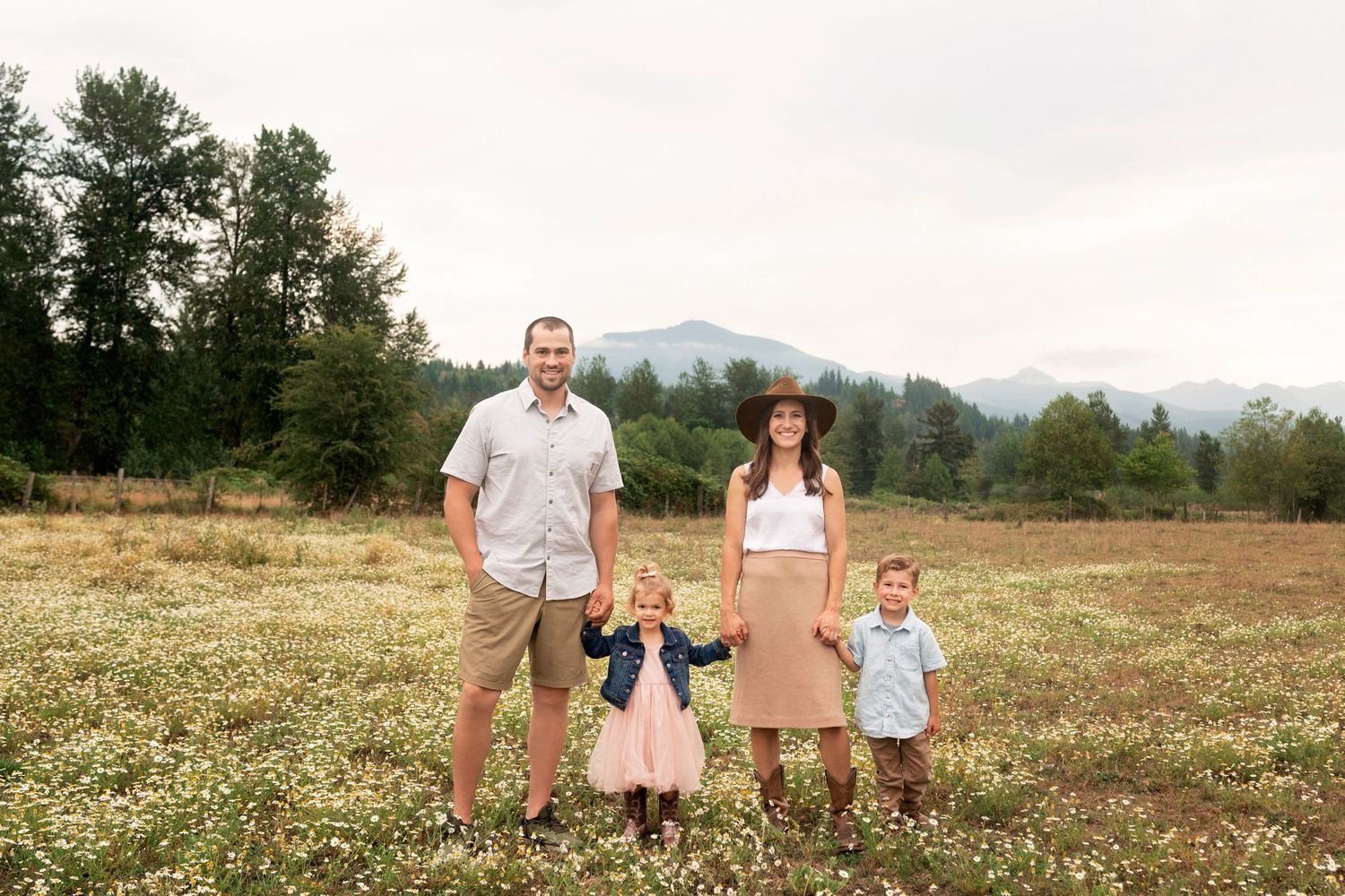 Family standing together in open field with mountain views in background.