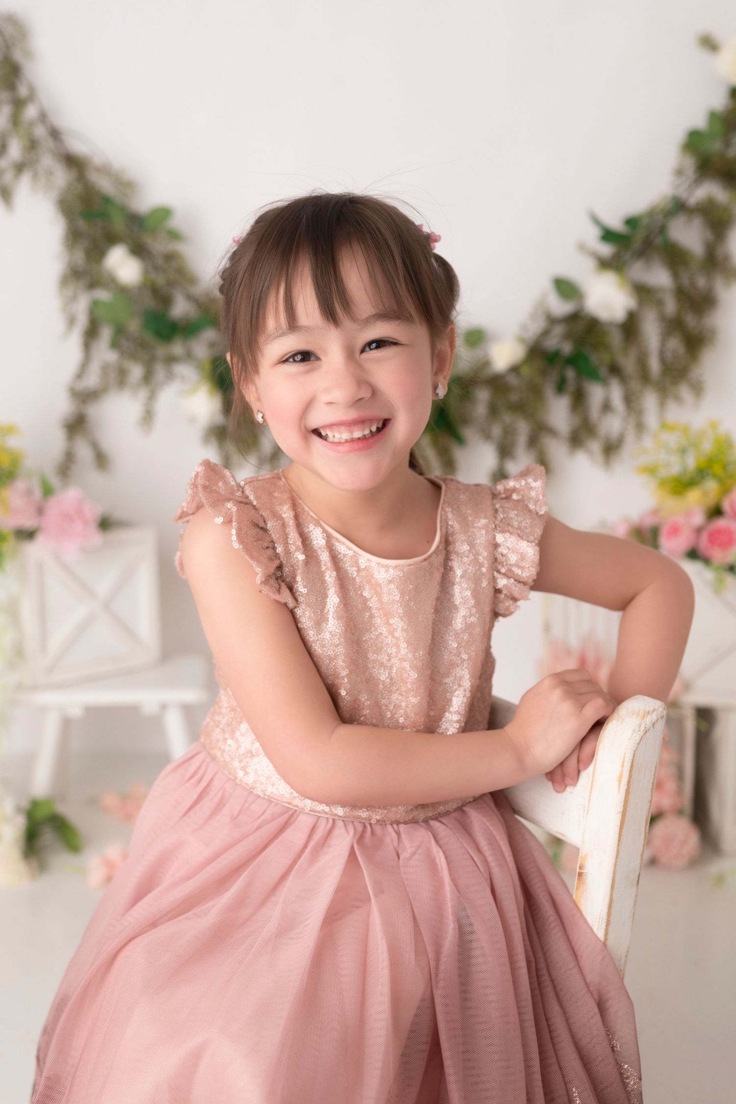 Little girl in pink tulle dress posing cheerfully against floral backdrop.
