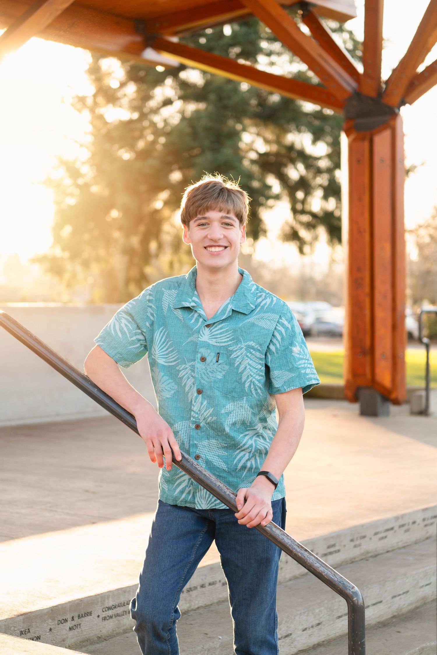 A student in a tropical print shirt stands under a wooden pavilion at sunset.