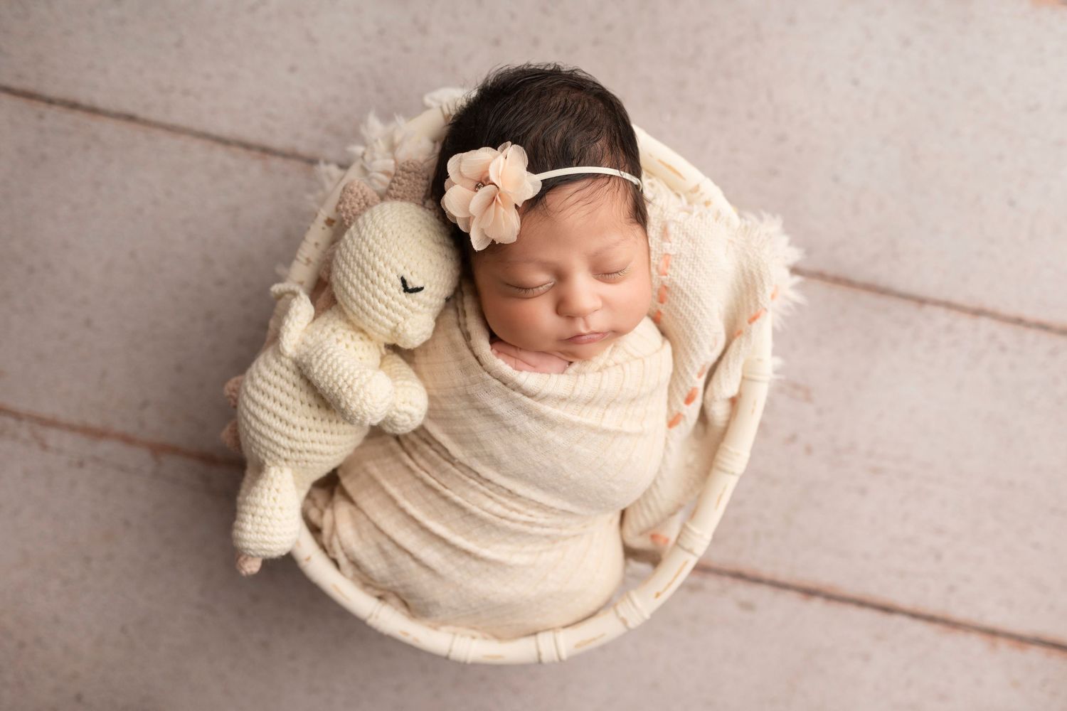 A collection of soft, cream-colored newborn photography poses on white wooden flooring.