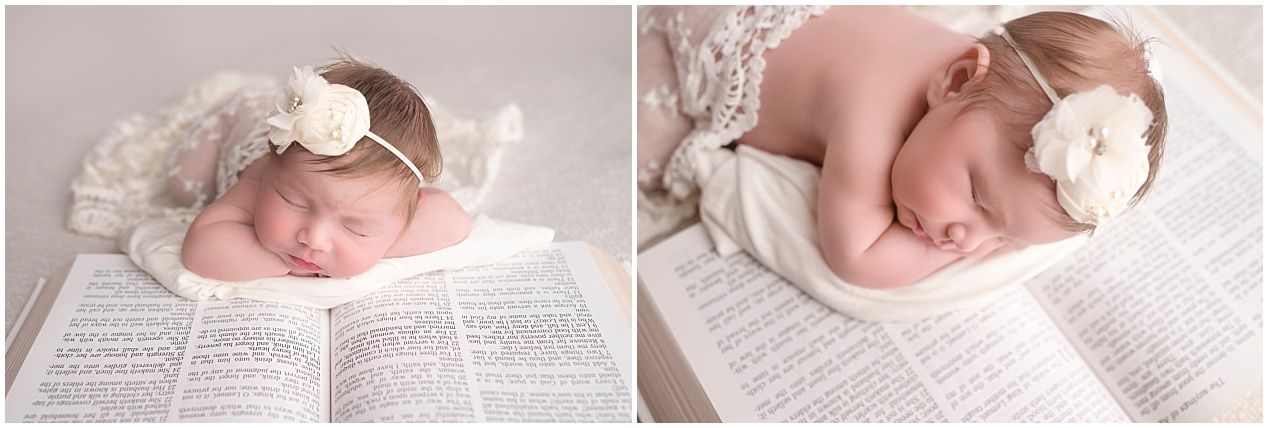 Newborn sleeping on open book with white bow headband accessory.