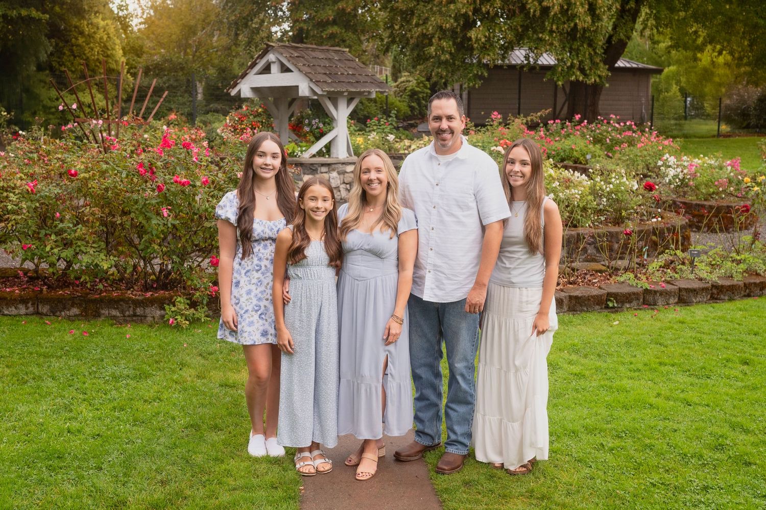 A group poses in coordinated pastel outfits in a garden with blooming roses.